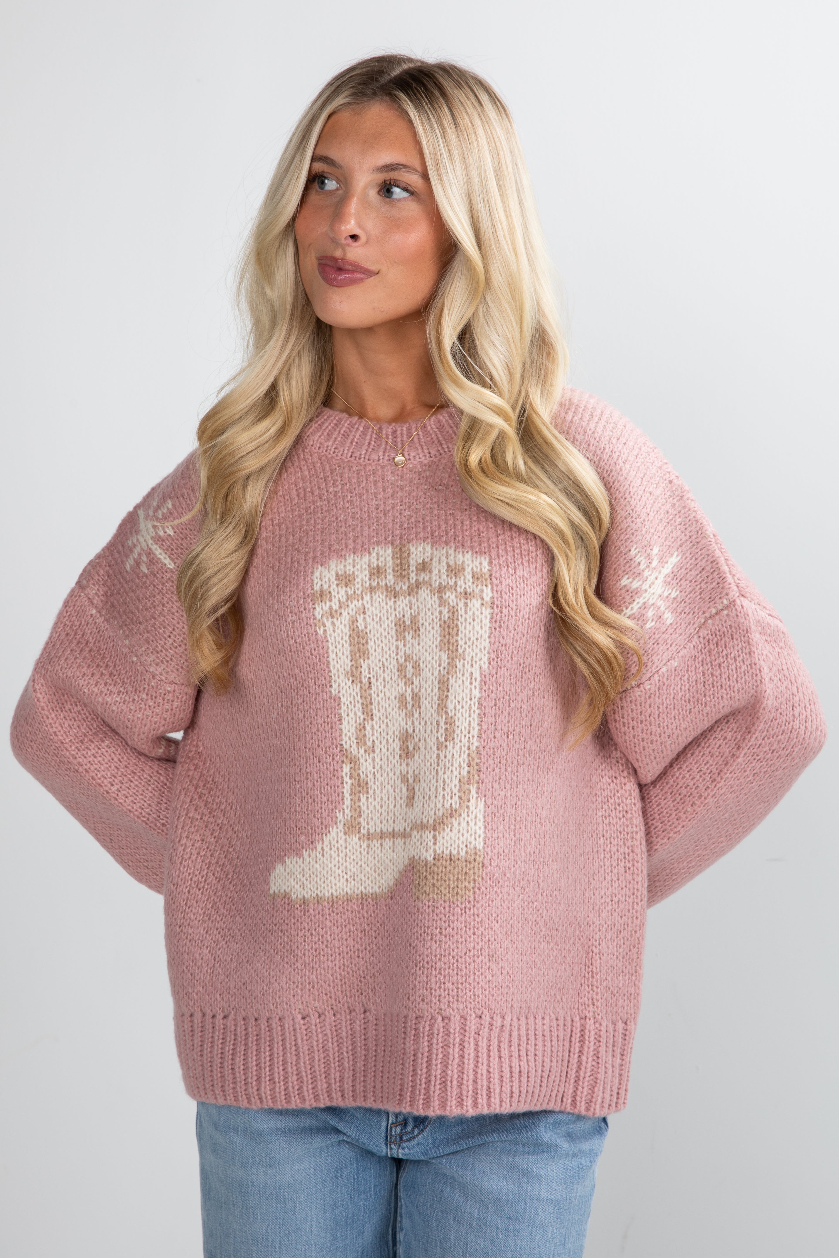 Woman wearing a pink sweater with a white boot design on a plain background