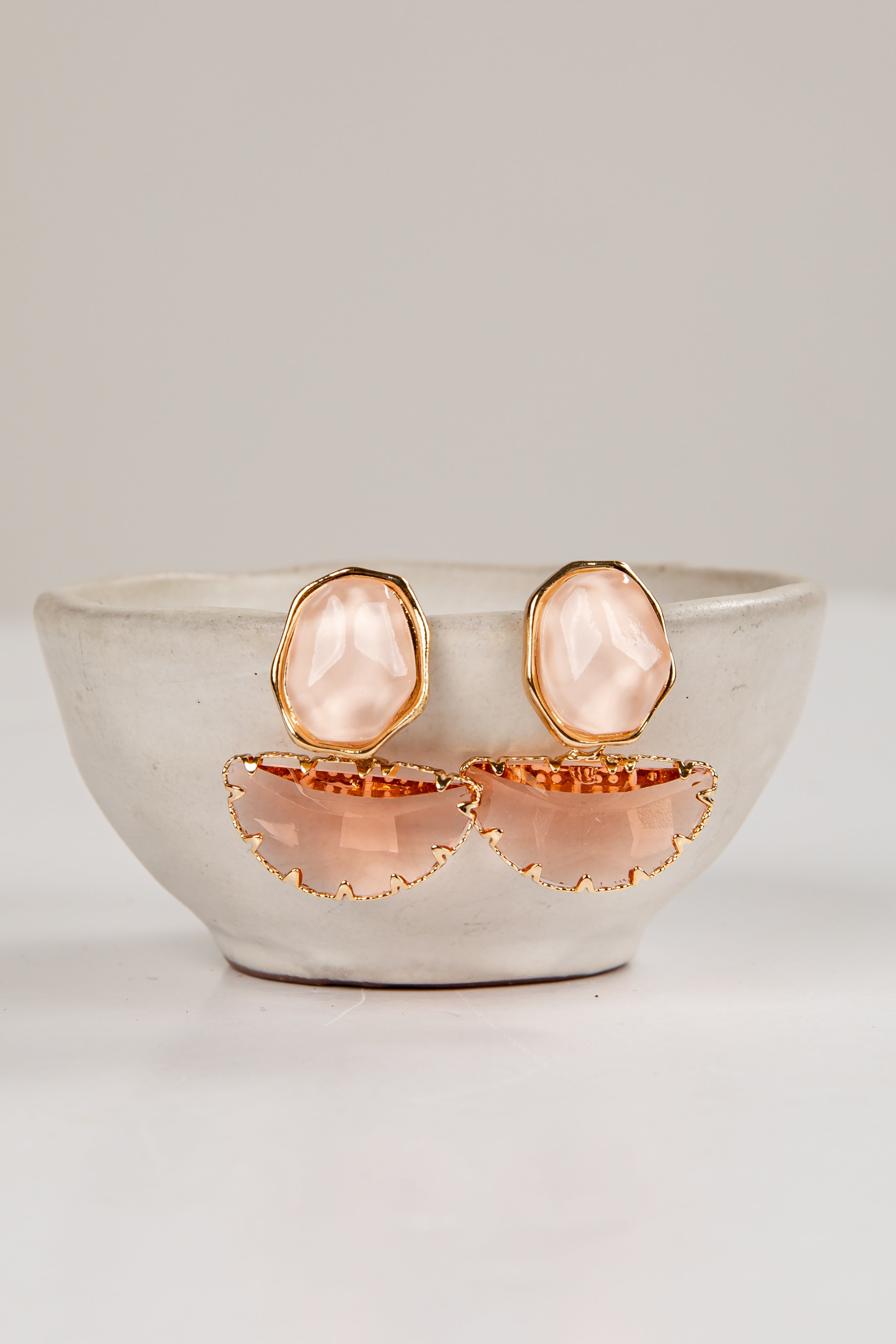 Rose gold earrings with pink stones in a white bowl on a light gray background