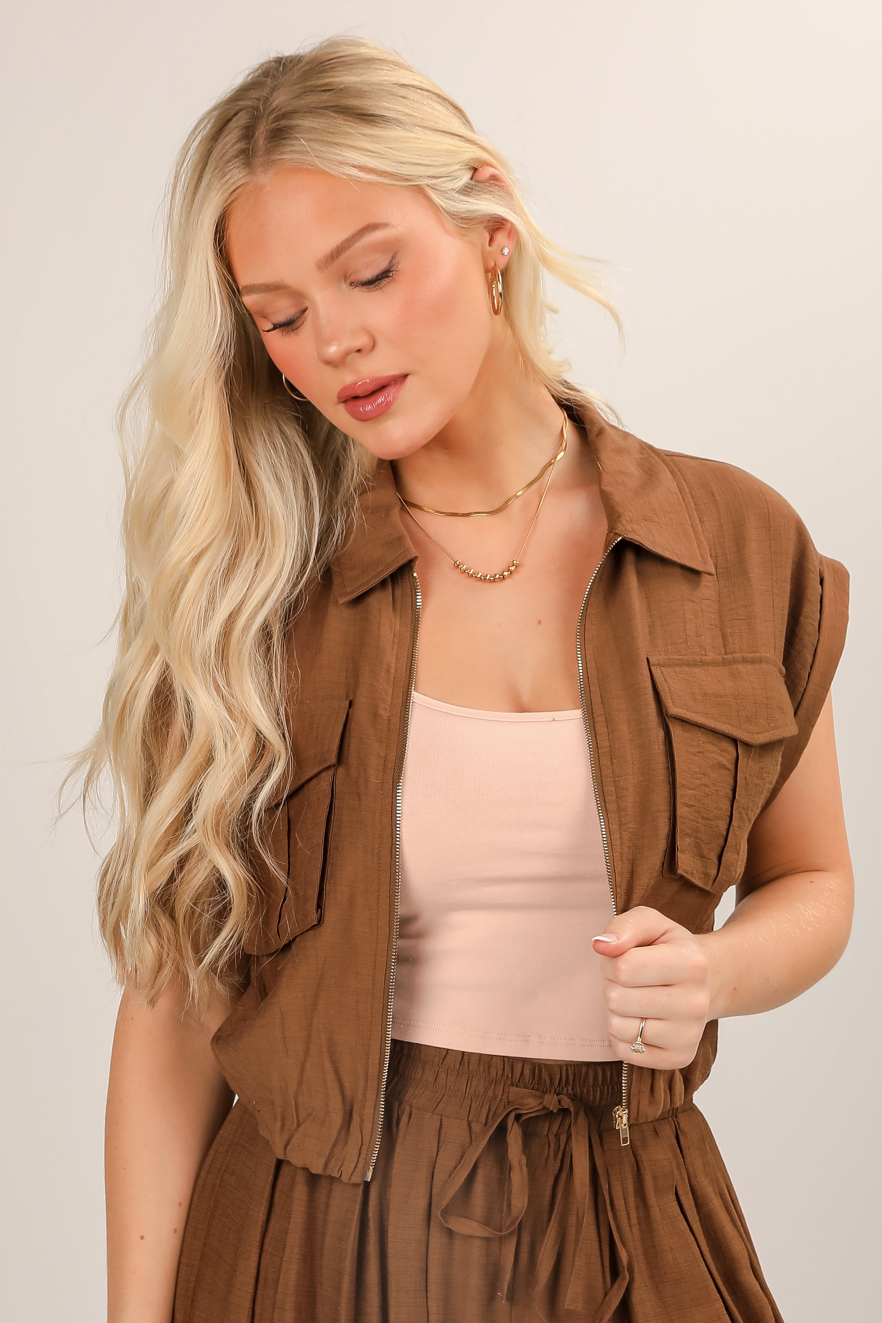 Woman wearing a brown vest over a pink top on a plain background