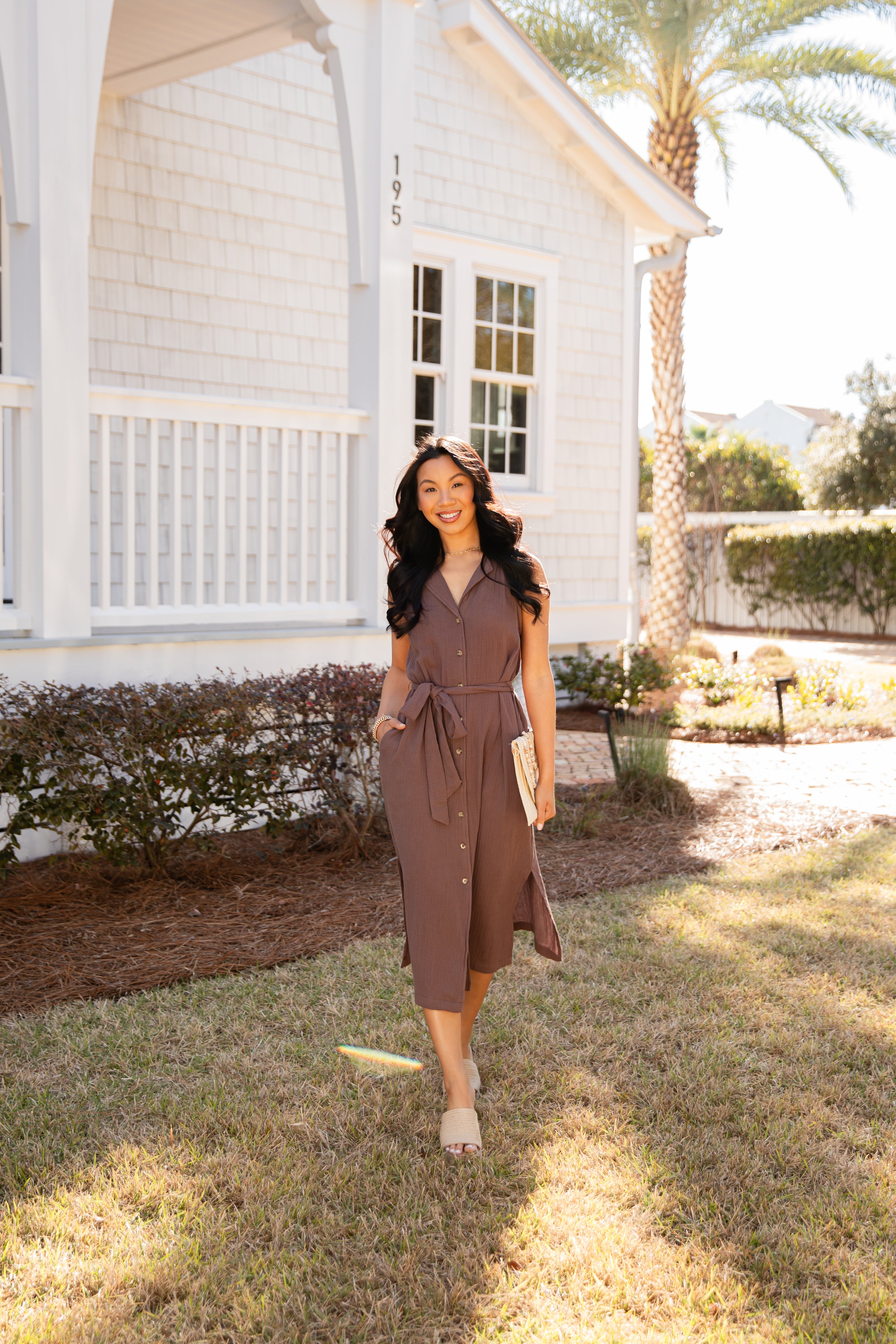 Woman in a brown dress standing in front of a white house with palm trees in the background