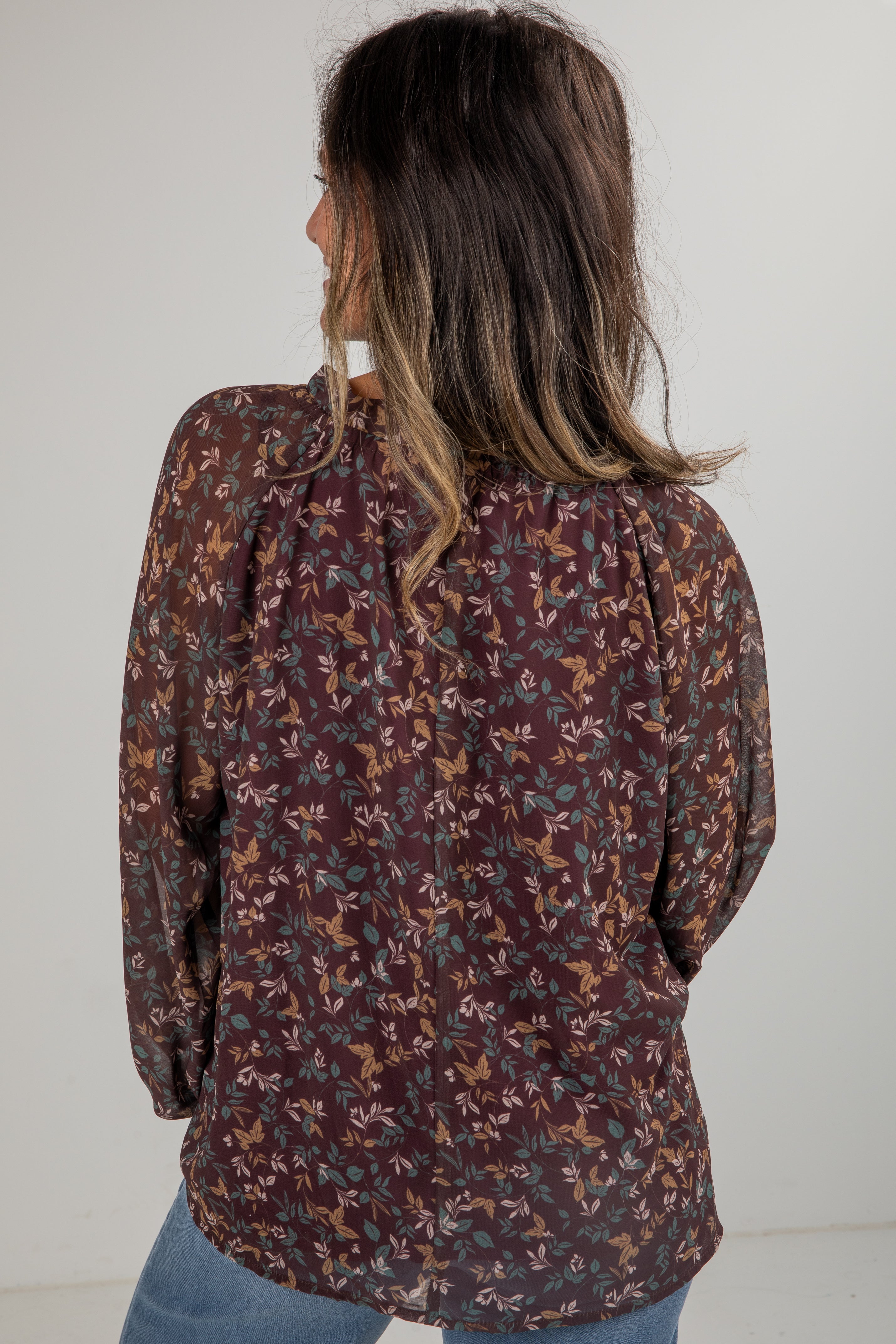 Woman wearing a patterned blouse with long sleeves against a plain background