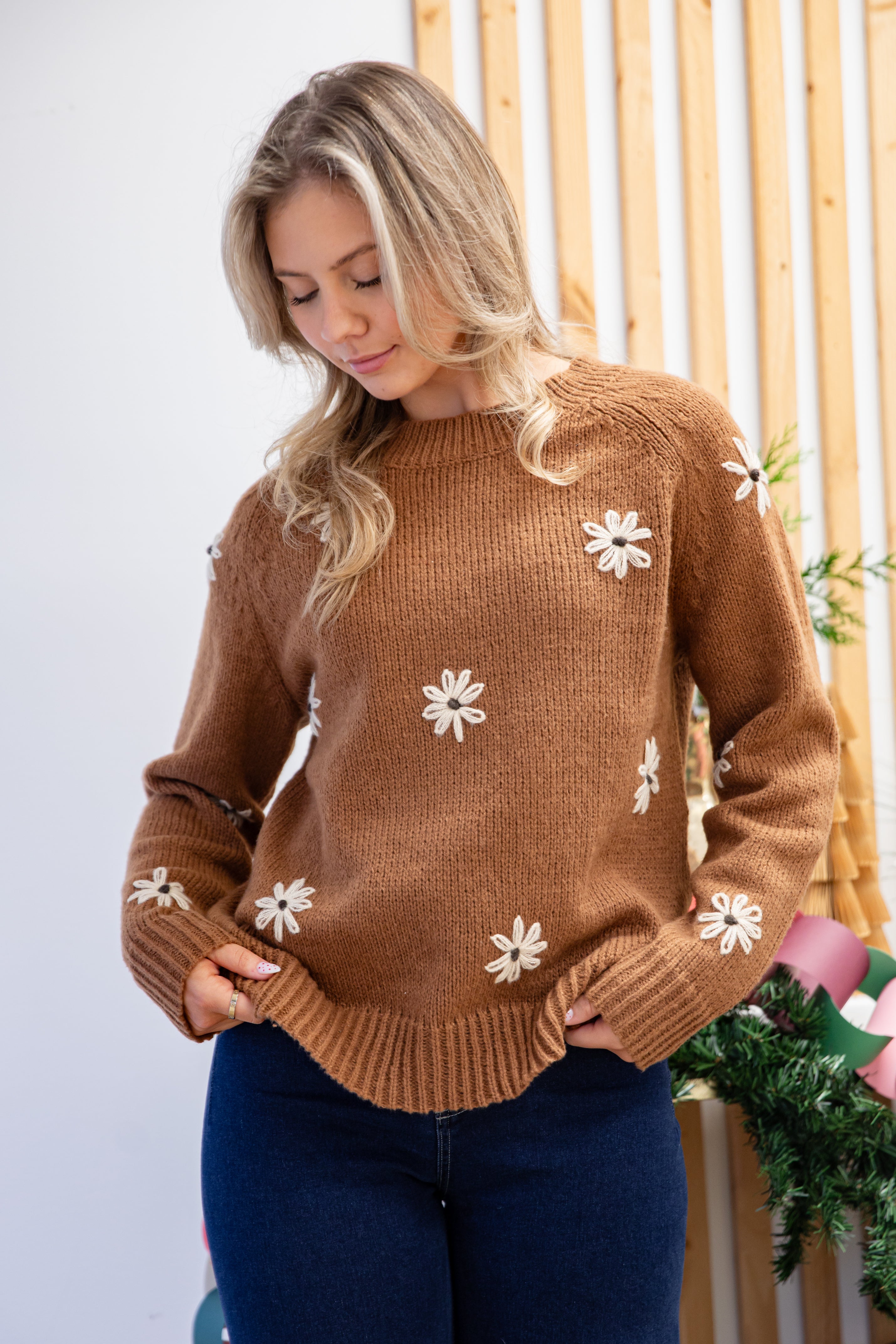 Woman wearing a brown sweater with white floral patterns against a light background