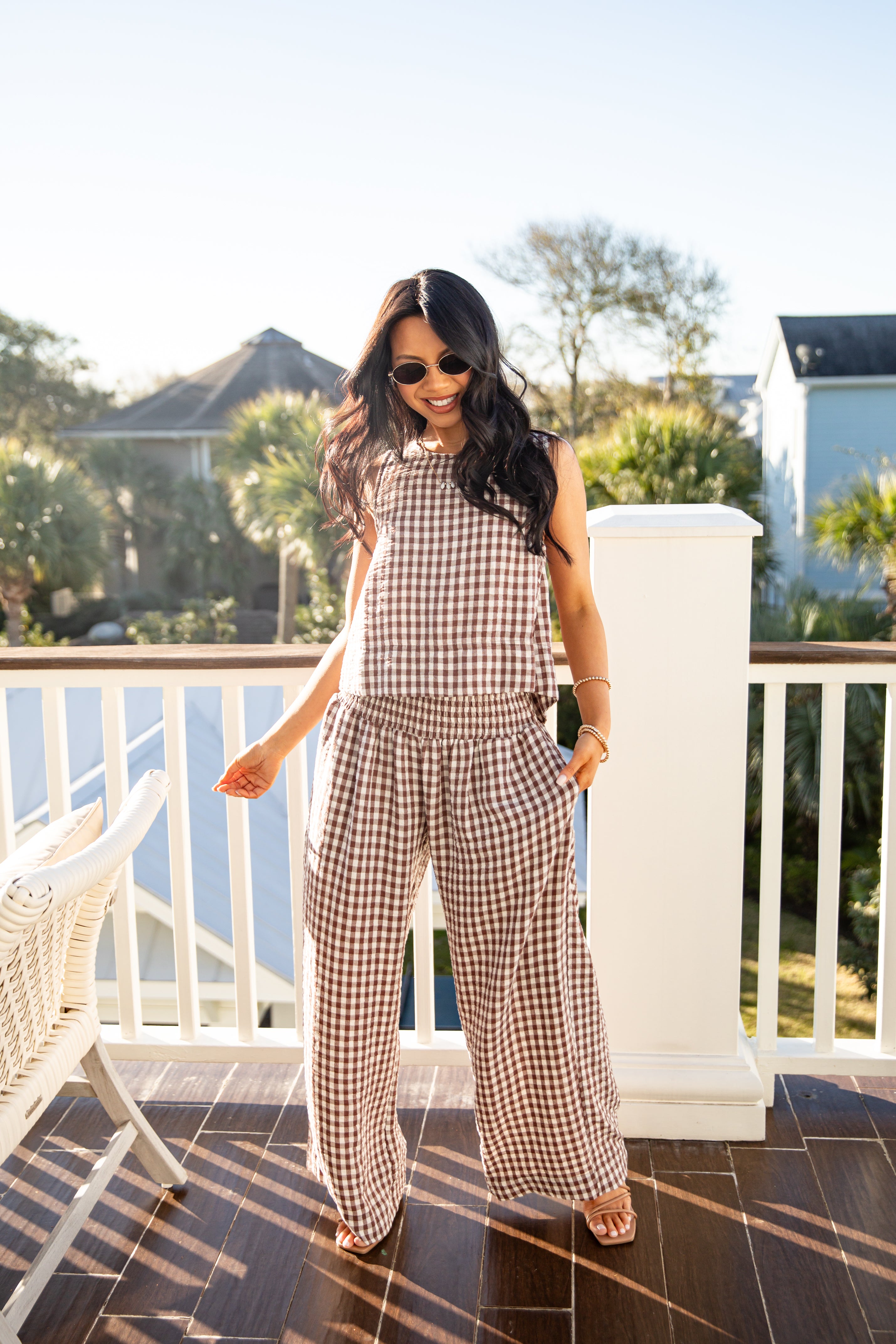 Woman in a checkered jumpsuit standing on a balcony with a scenic background