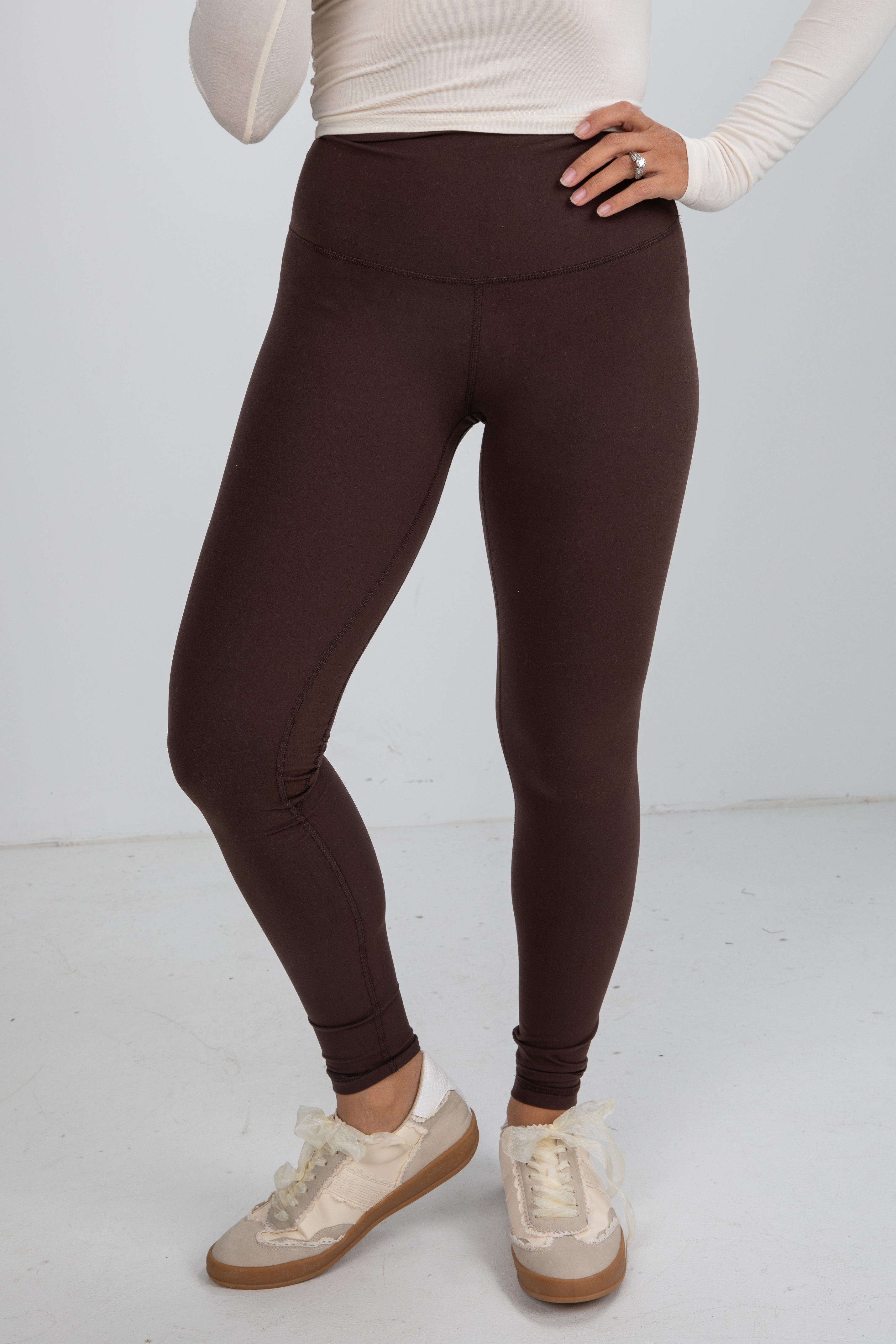Person wearing brown leggings and white sneakers on a light gray background