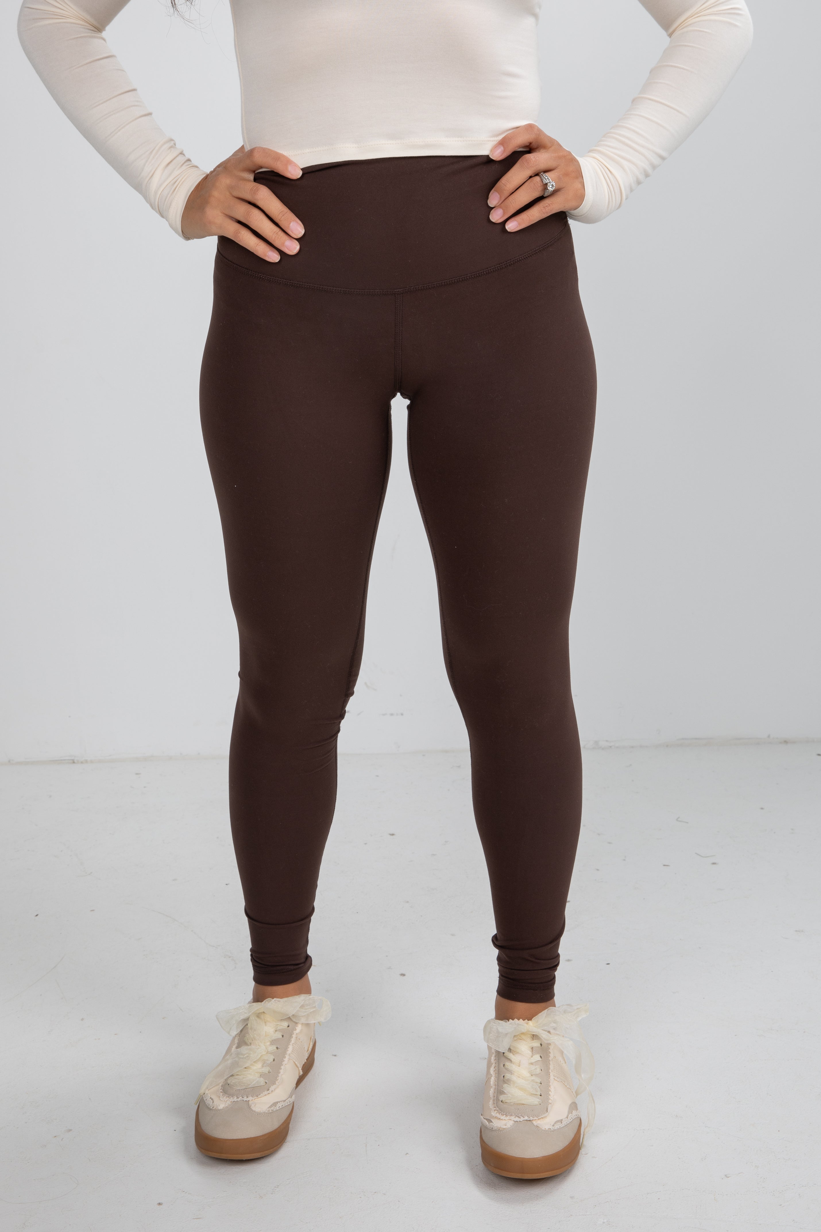 Person wearing brown leggings and white sneakers on a white background