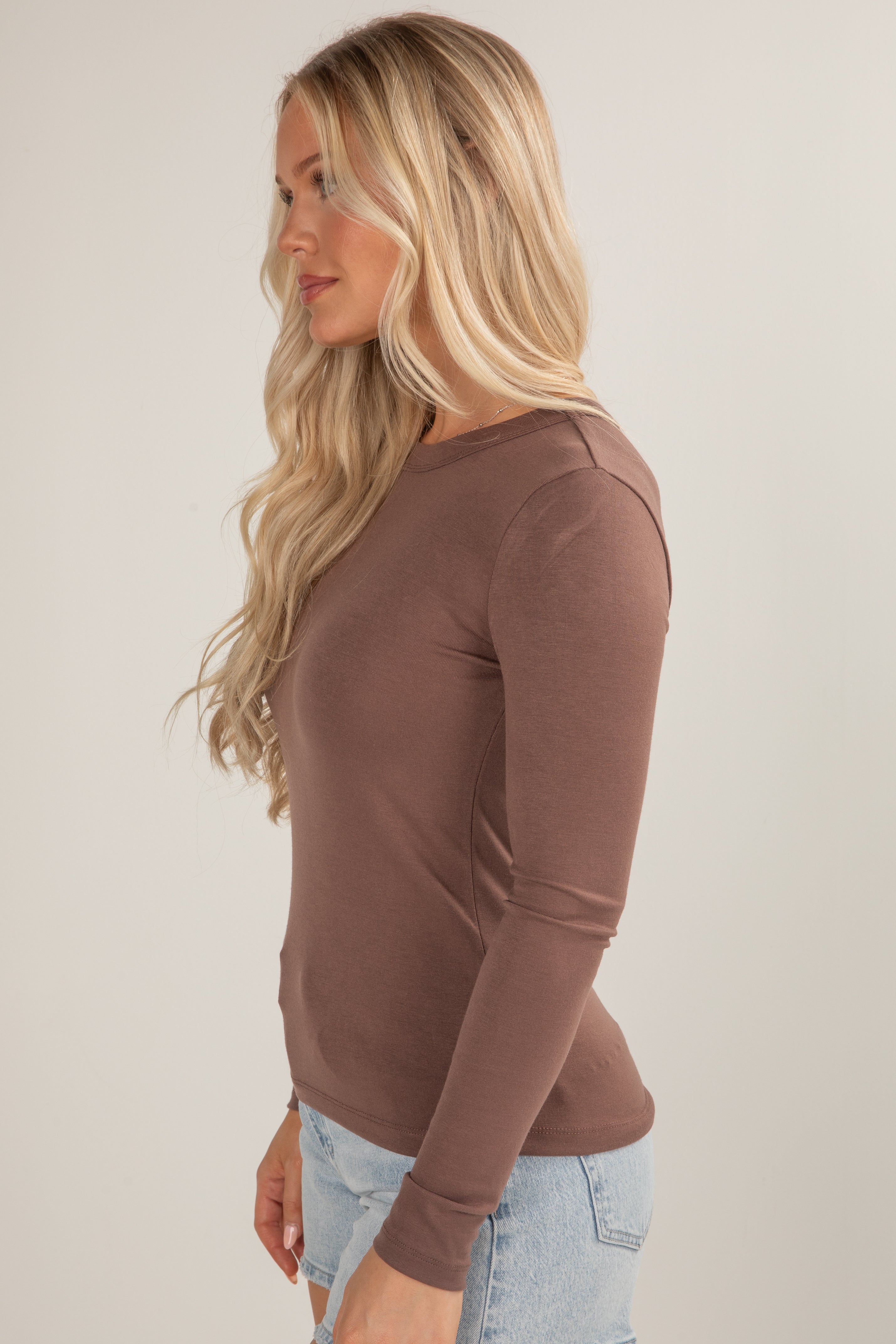 Woman wearing a brown long-sleeve top against a plain background