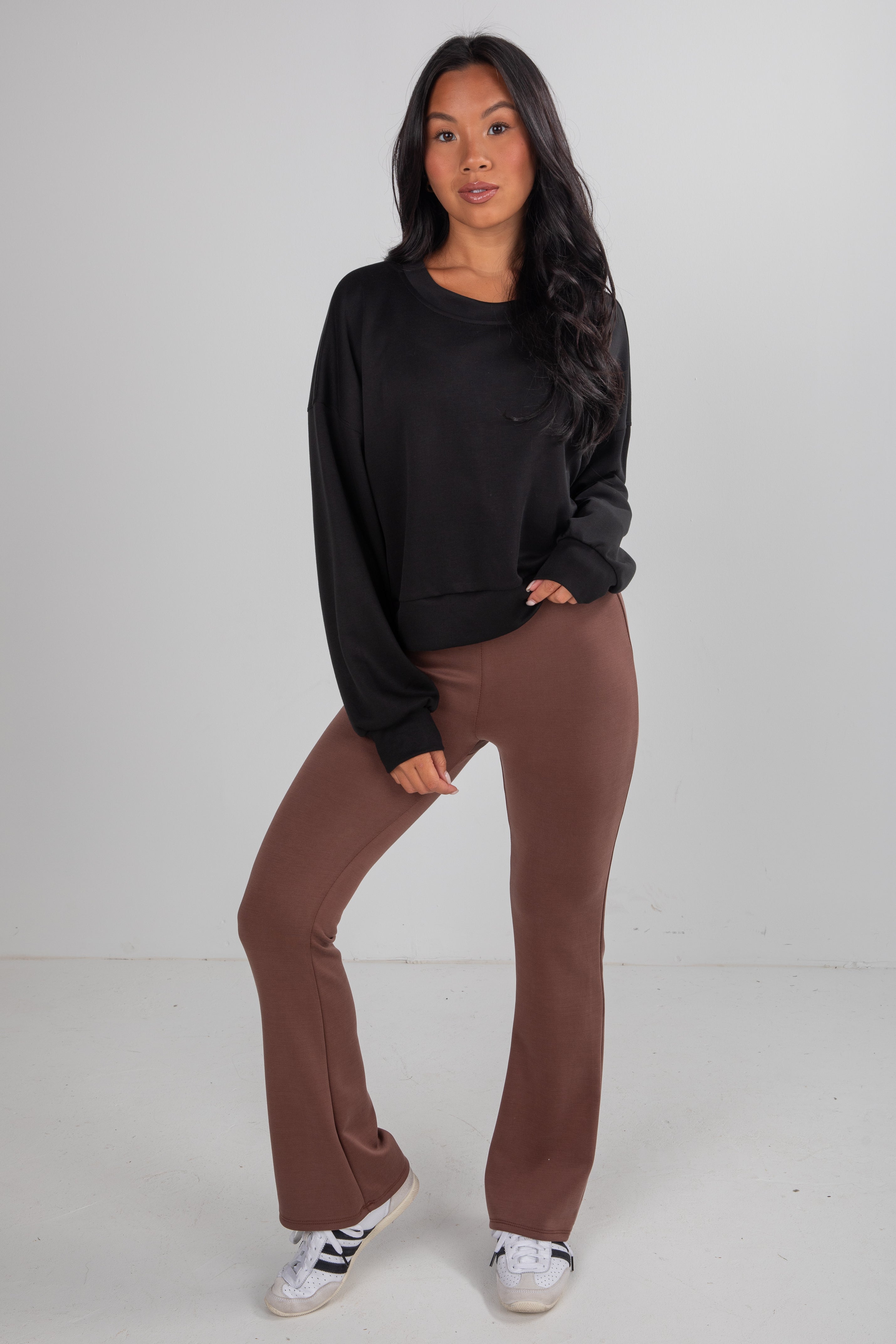 Woman wearing a black sweatshirt and brown pants on a white background