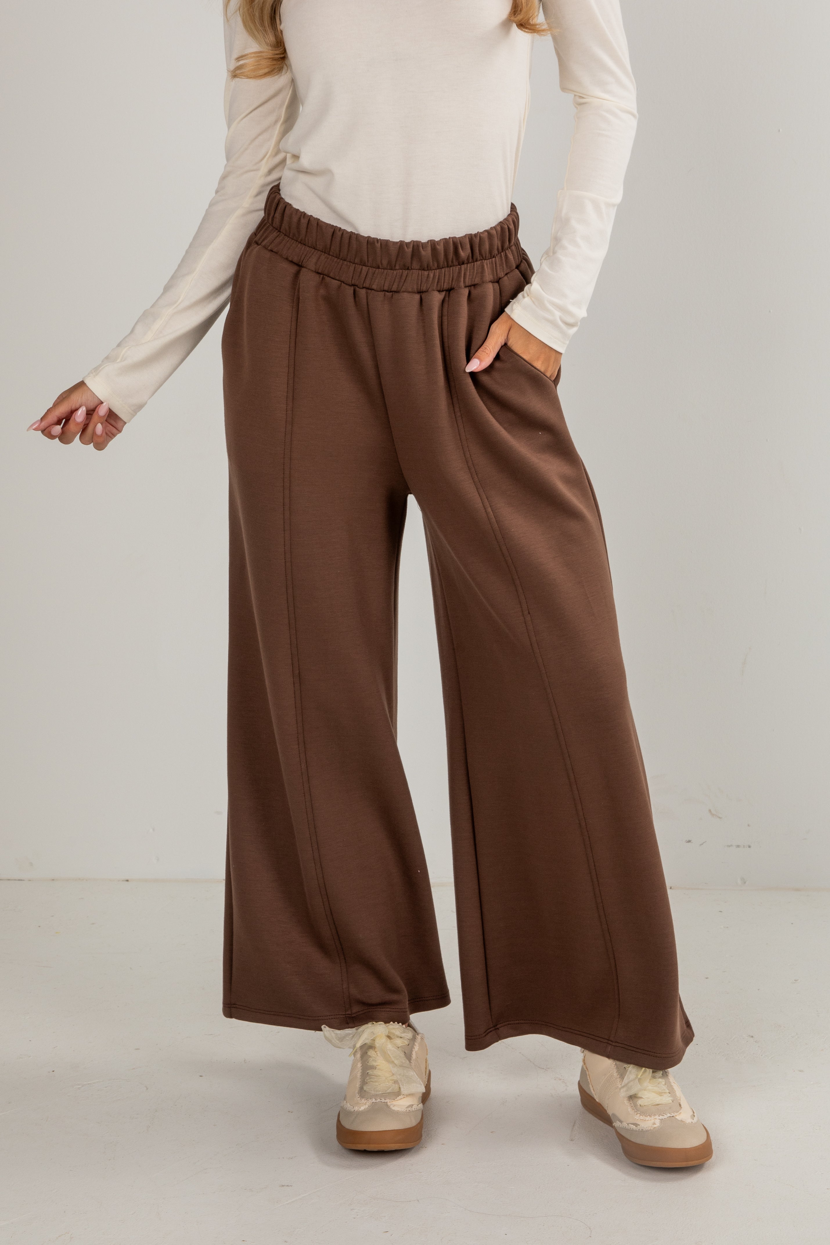 Person wearing brown wide-leg pants and a beige top on a plain background