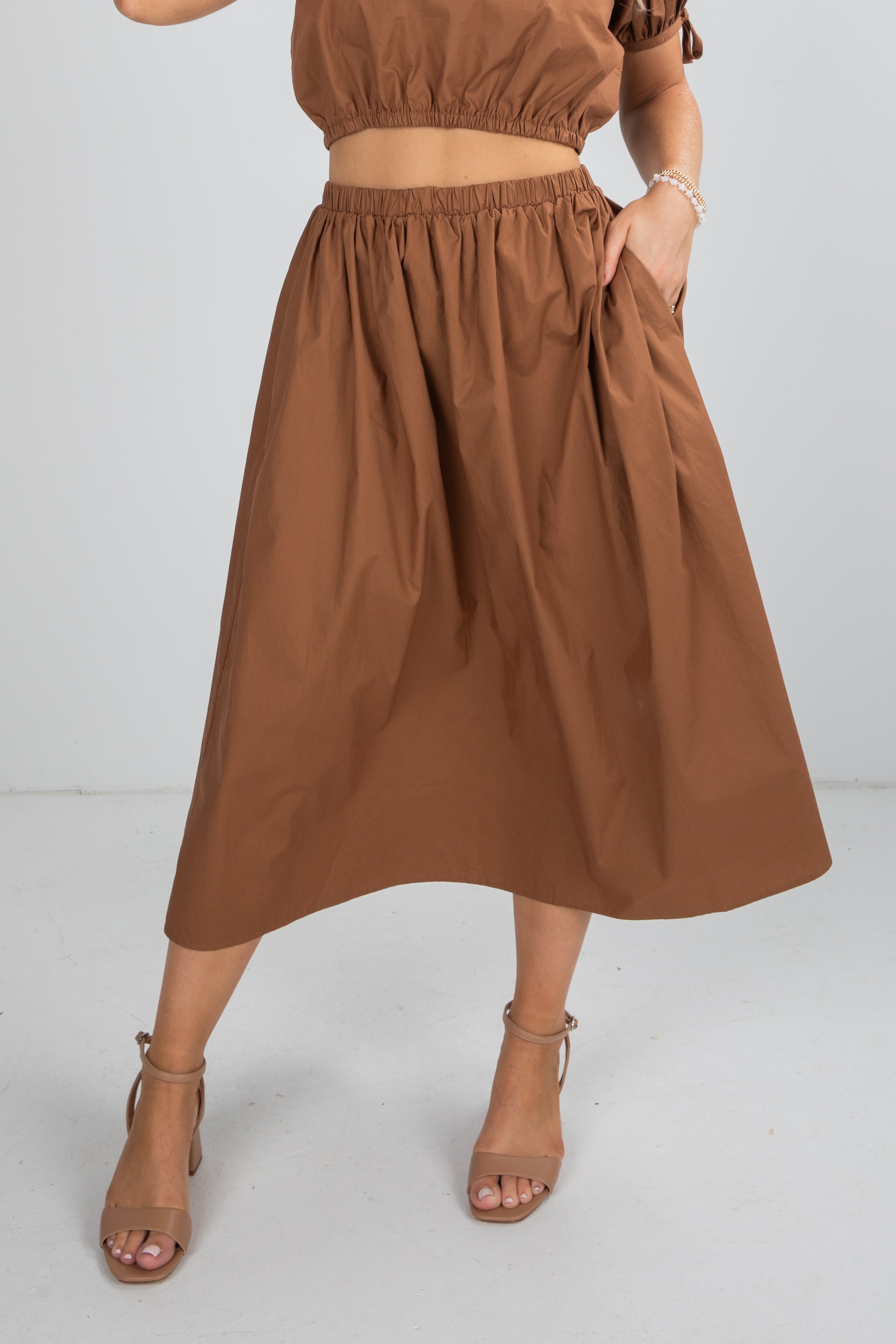 Person wearing a brown outfit with a top and skirt on a white background