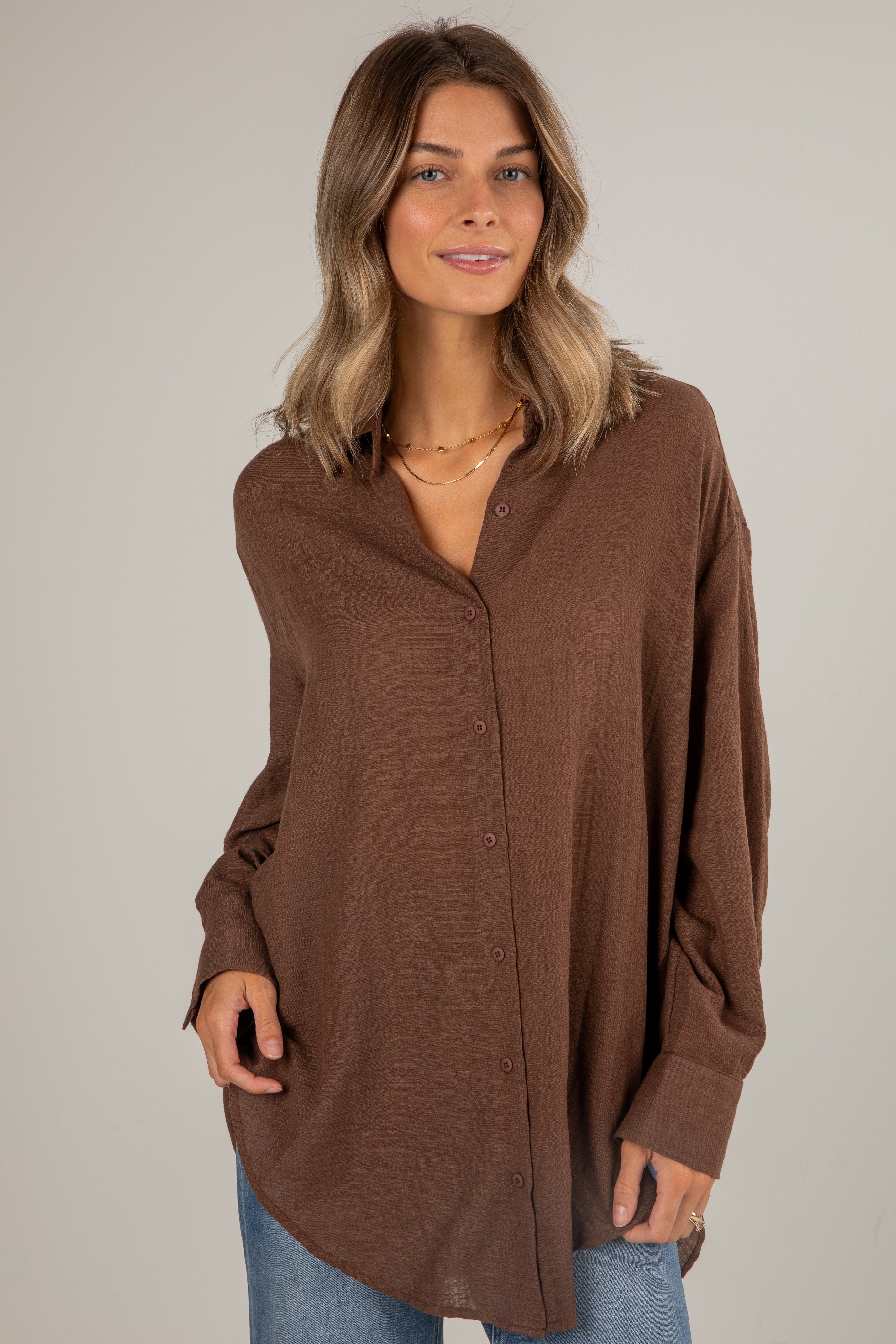 Woman wearing a brown button-up shirt against a plain background
