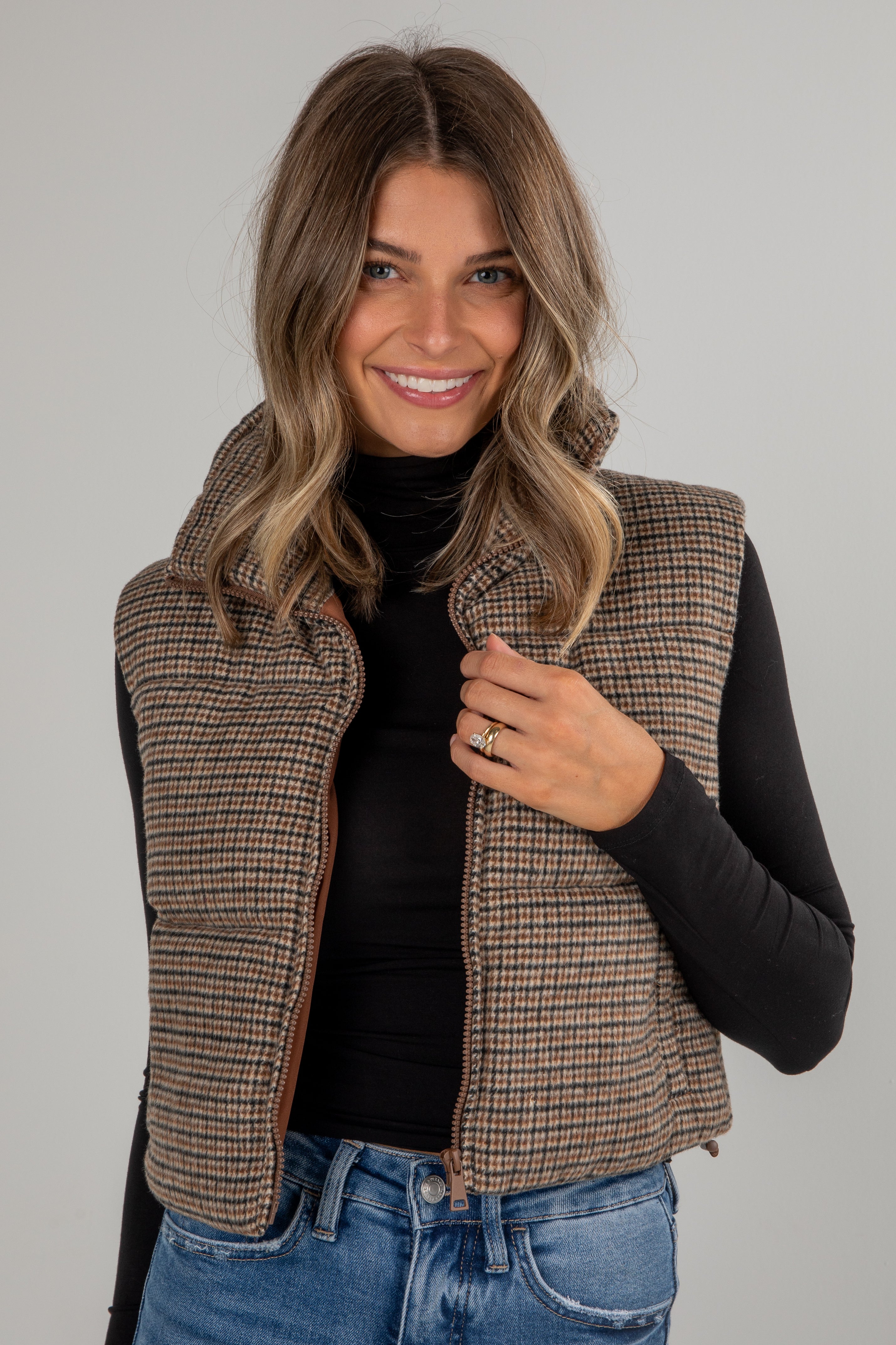 Woman wearing a plaid vest over a black top and blue jeans on a gray background