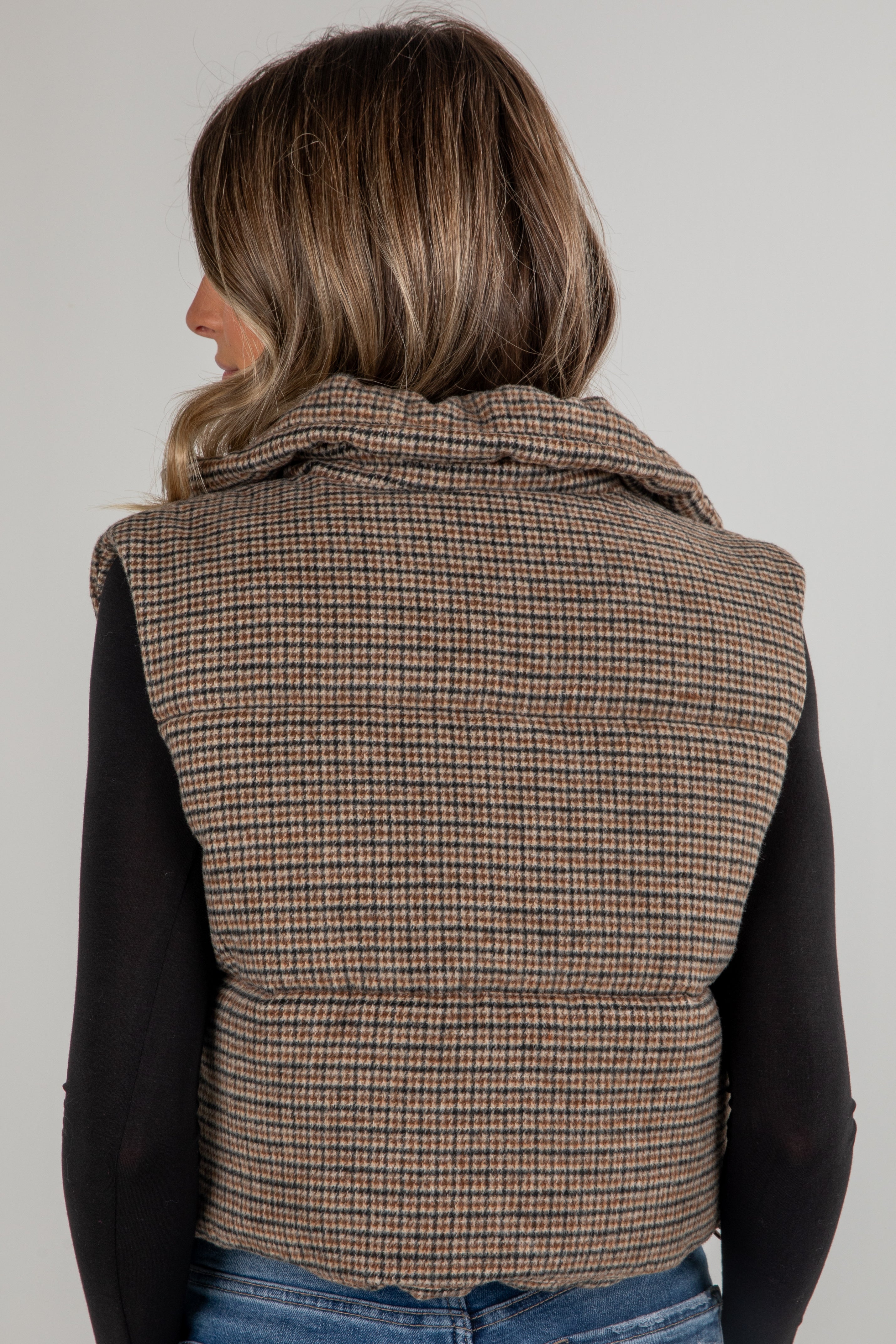 Person wearing a plaid vest over a black shirt on a plain background