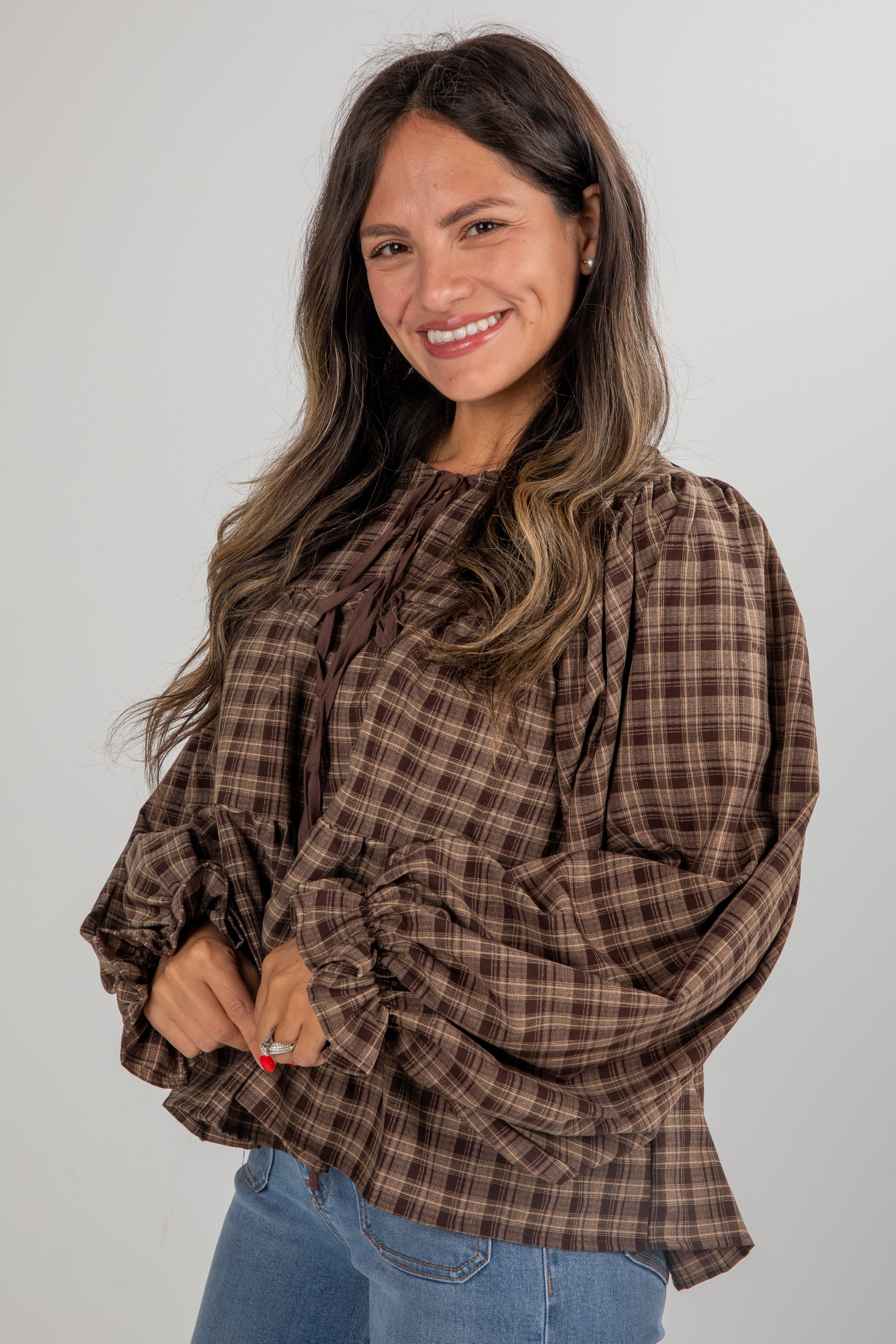 Woman wearing a brown plaid blouse with ruffled sleeves against a plain background