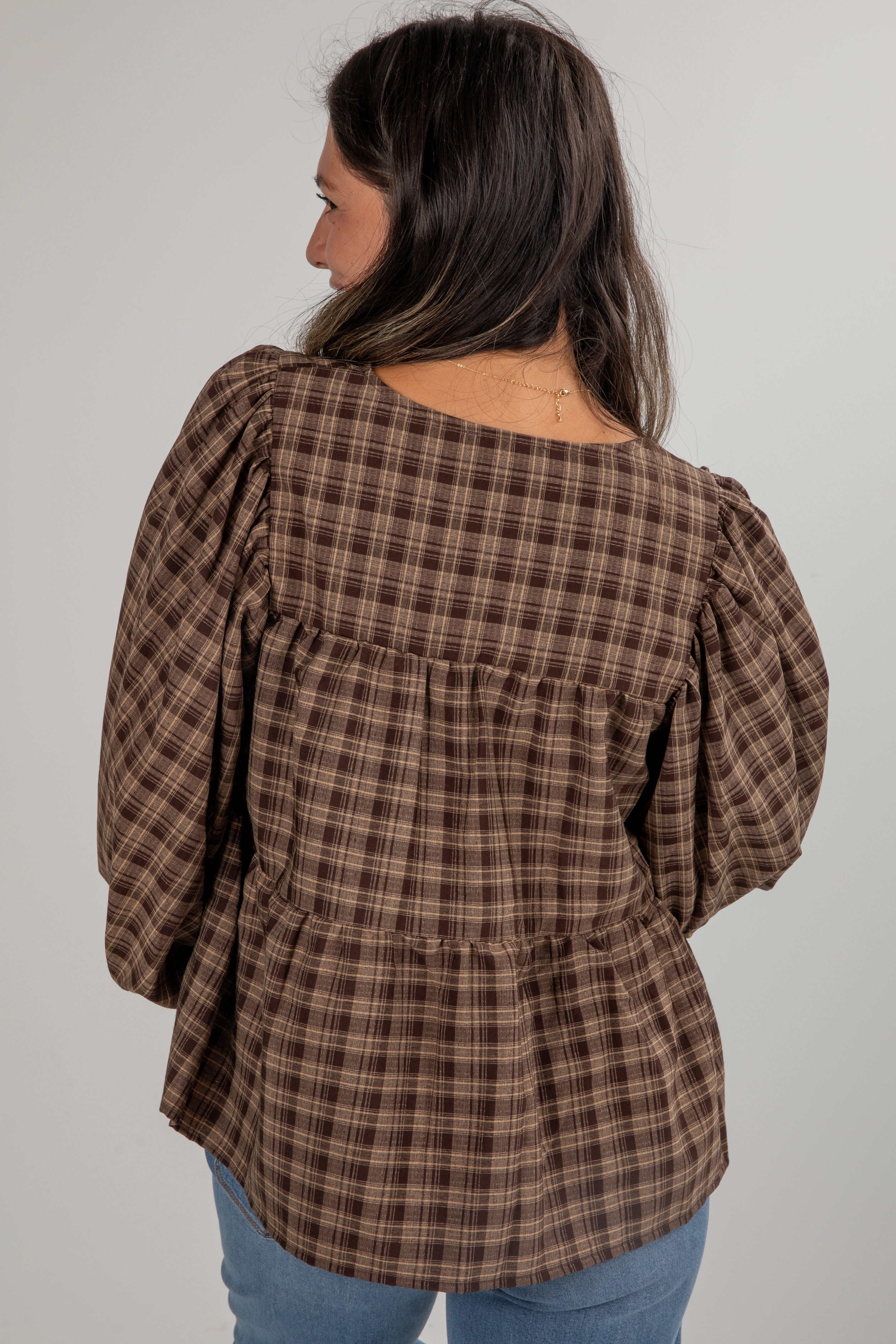Woman wearing a brown plaid blouse with puffed sleeves on a plain background