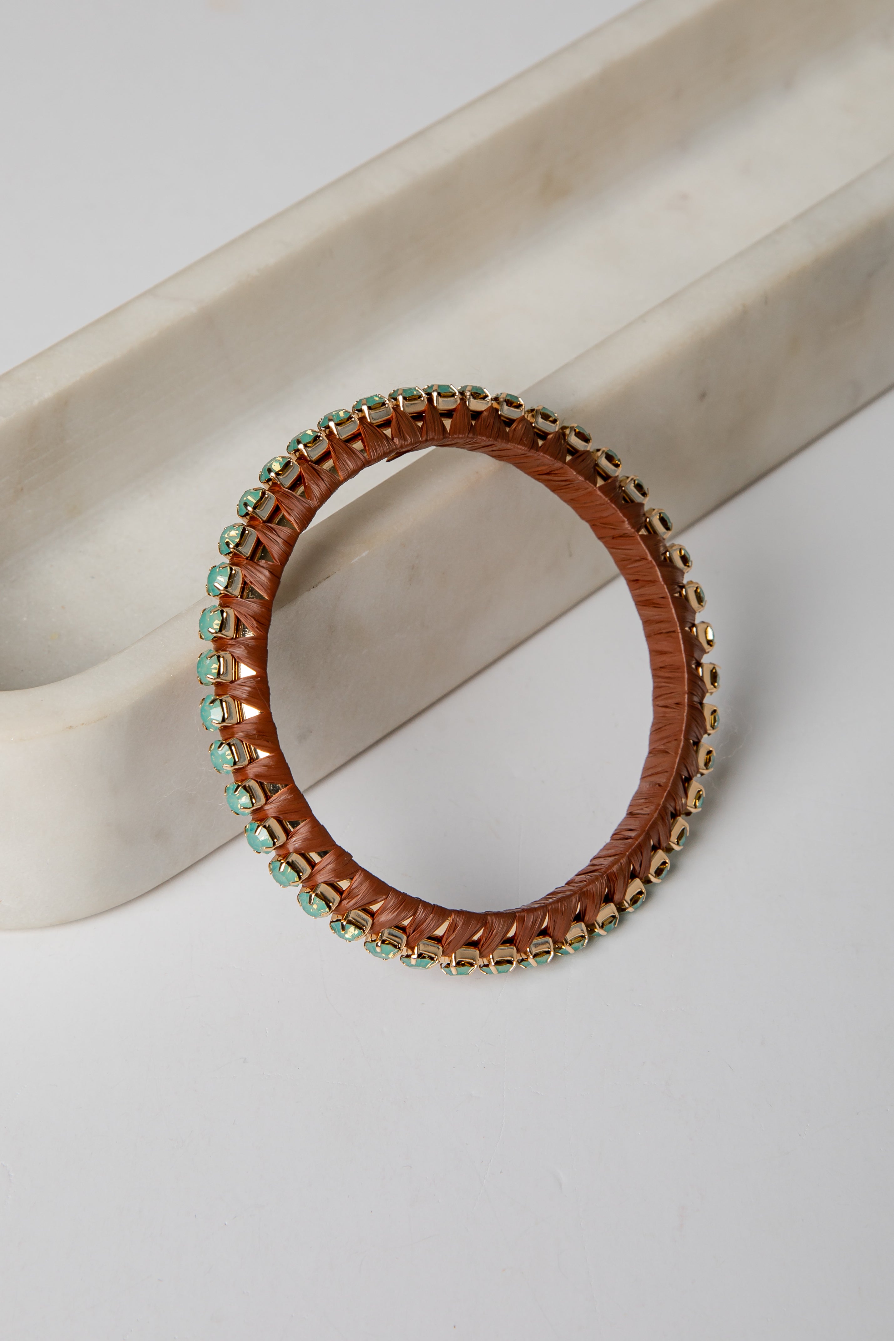 Brown leather bracelet with green beads on a light beige surface