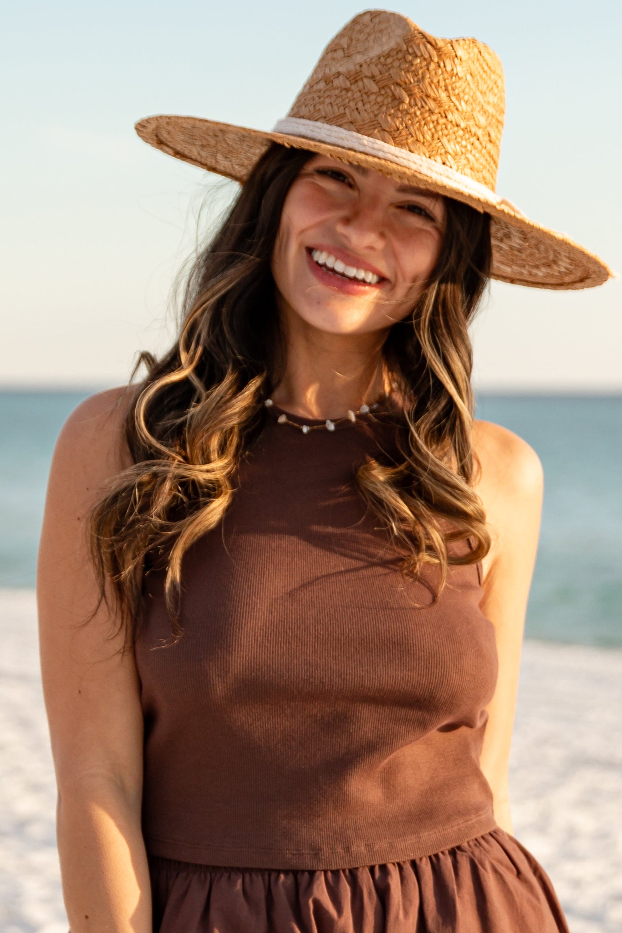 Woman wearing a brown dress and straw hat on a beach