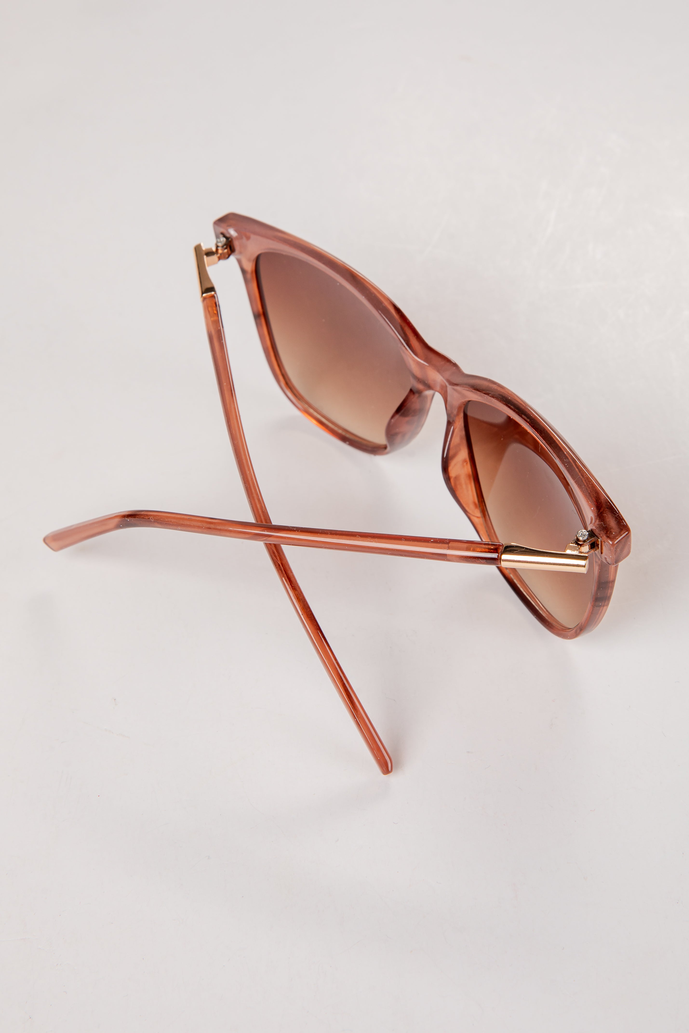 Rose gold sunglasses with brown lenses on a light gray background