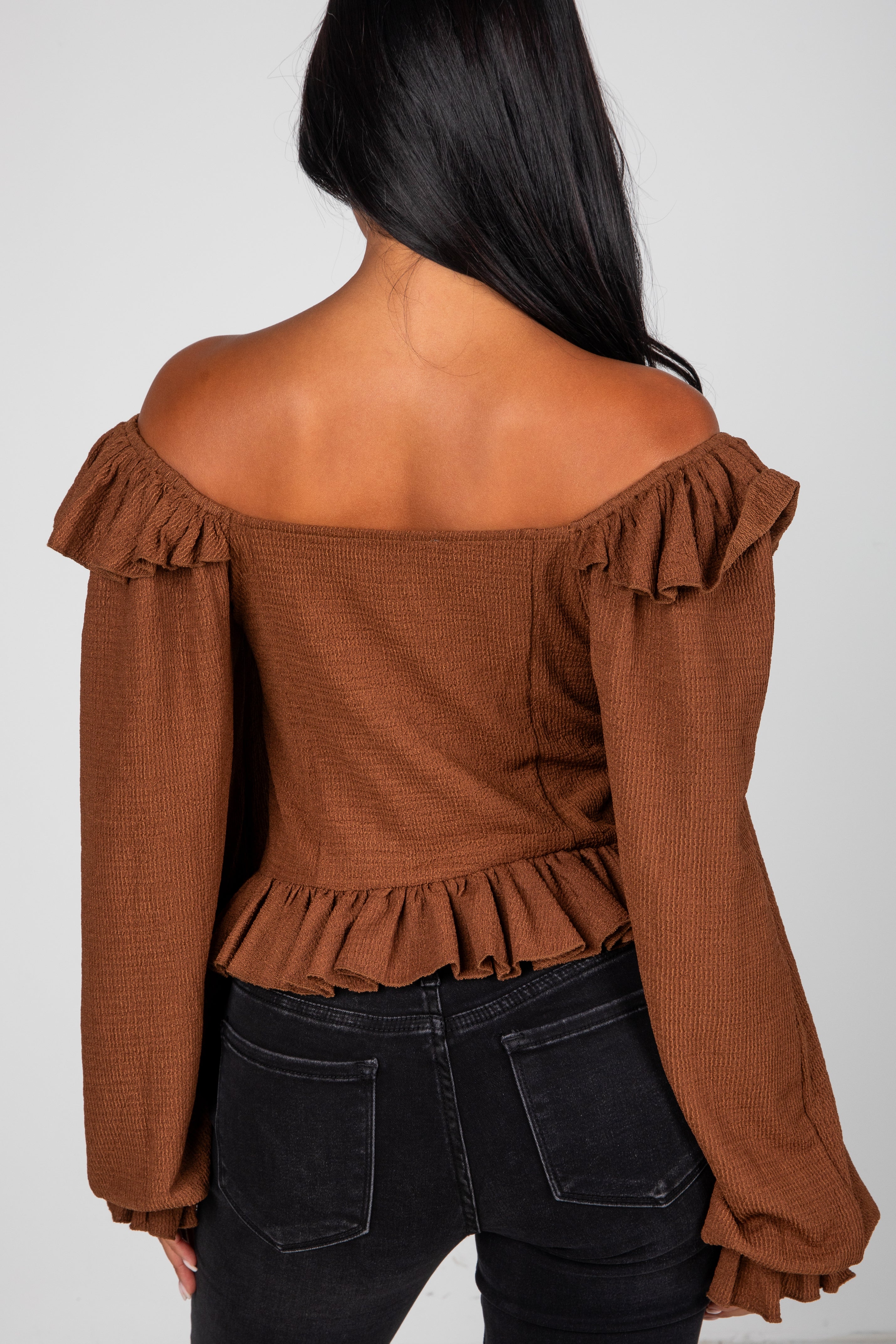 Brown off-shoulder top with ruffled details worn by a person on a plain background