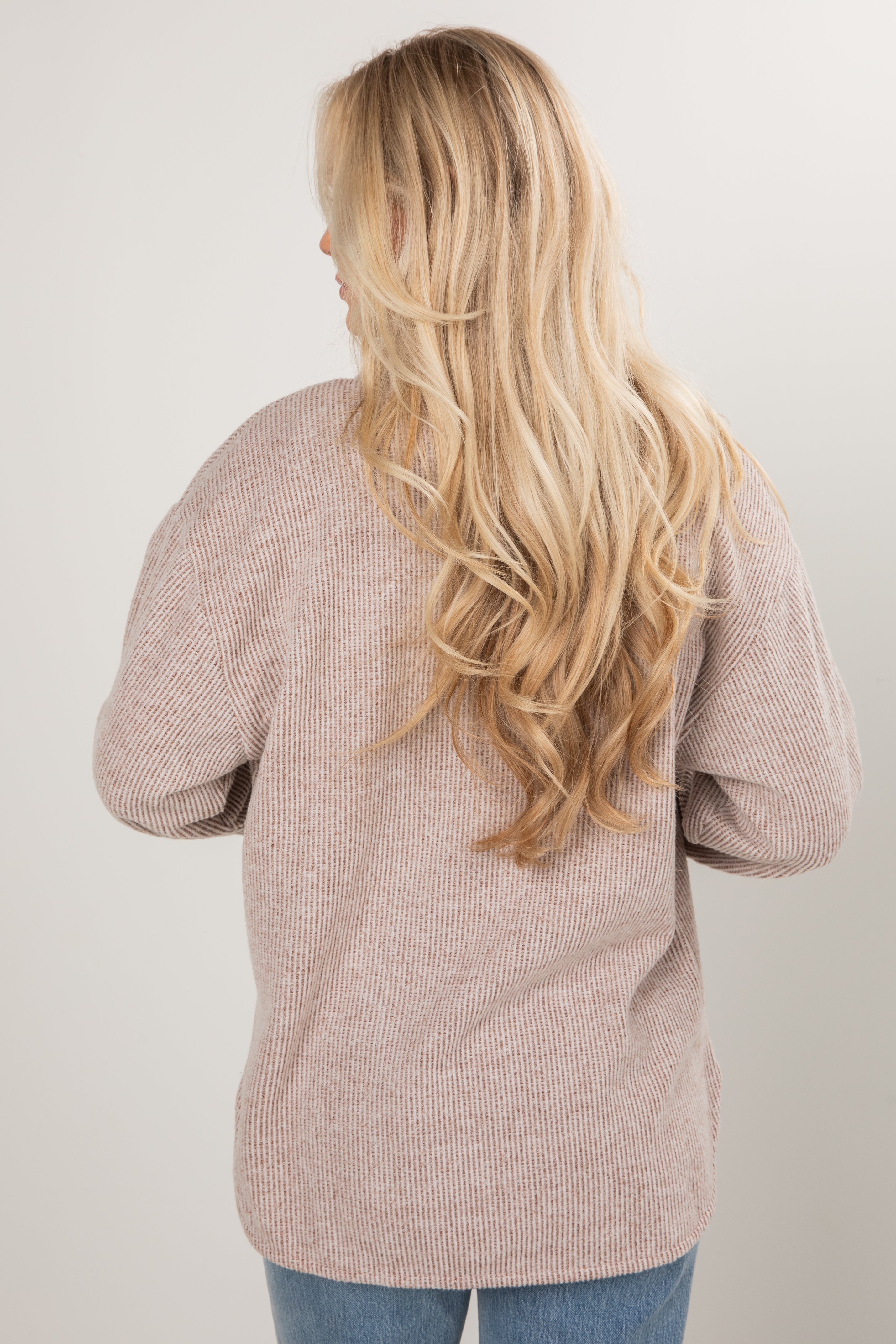 Person wearing a beige sweater with long blonde hair on a plain background