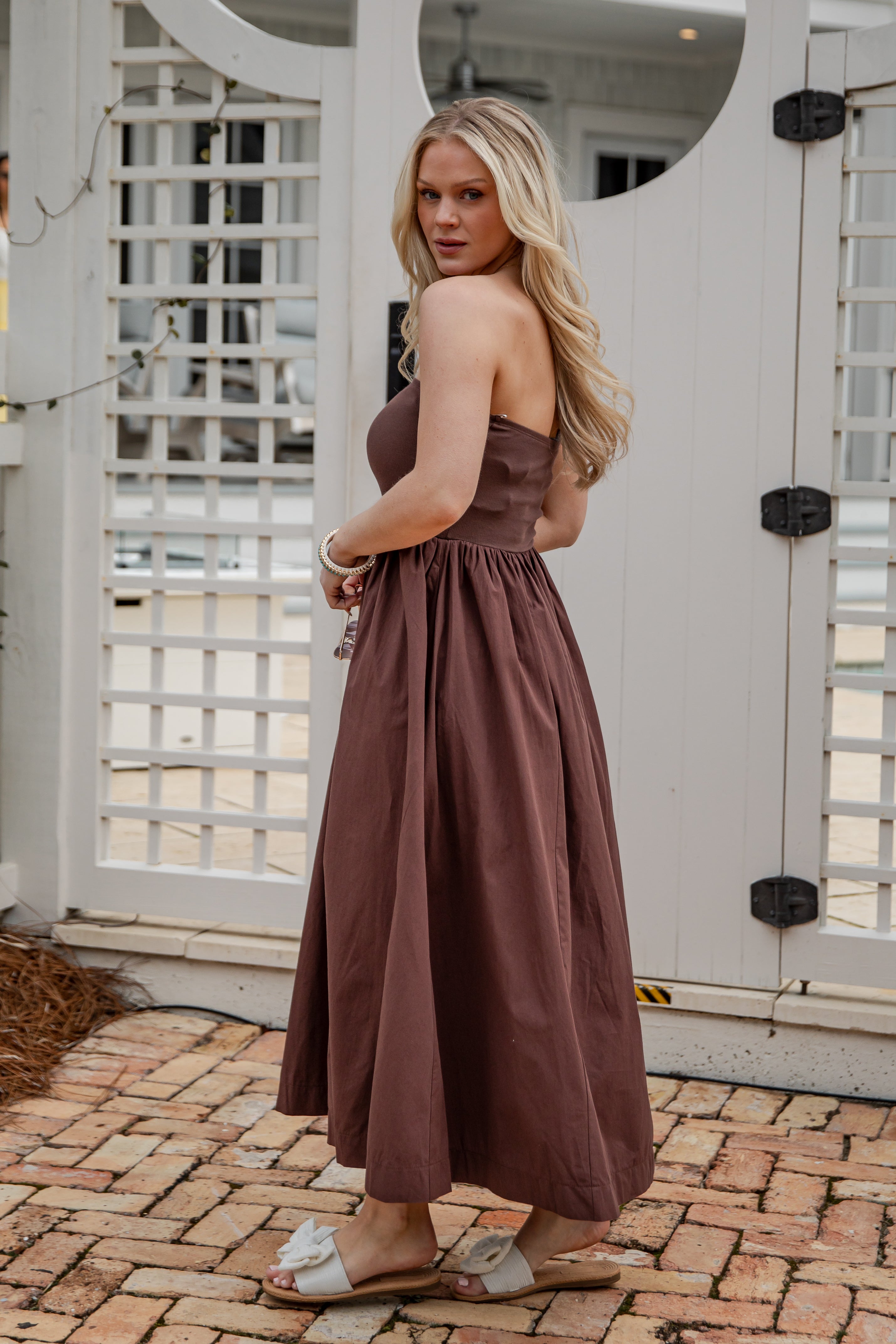 Woman in a brown strapless dress standing in front of a white lattice door.