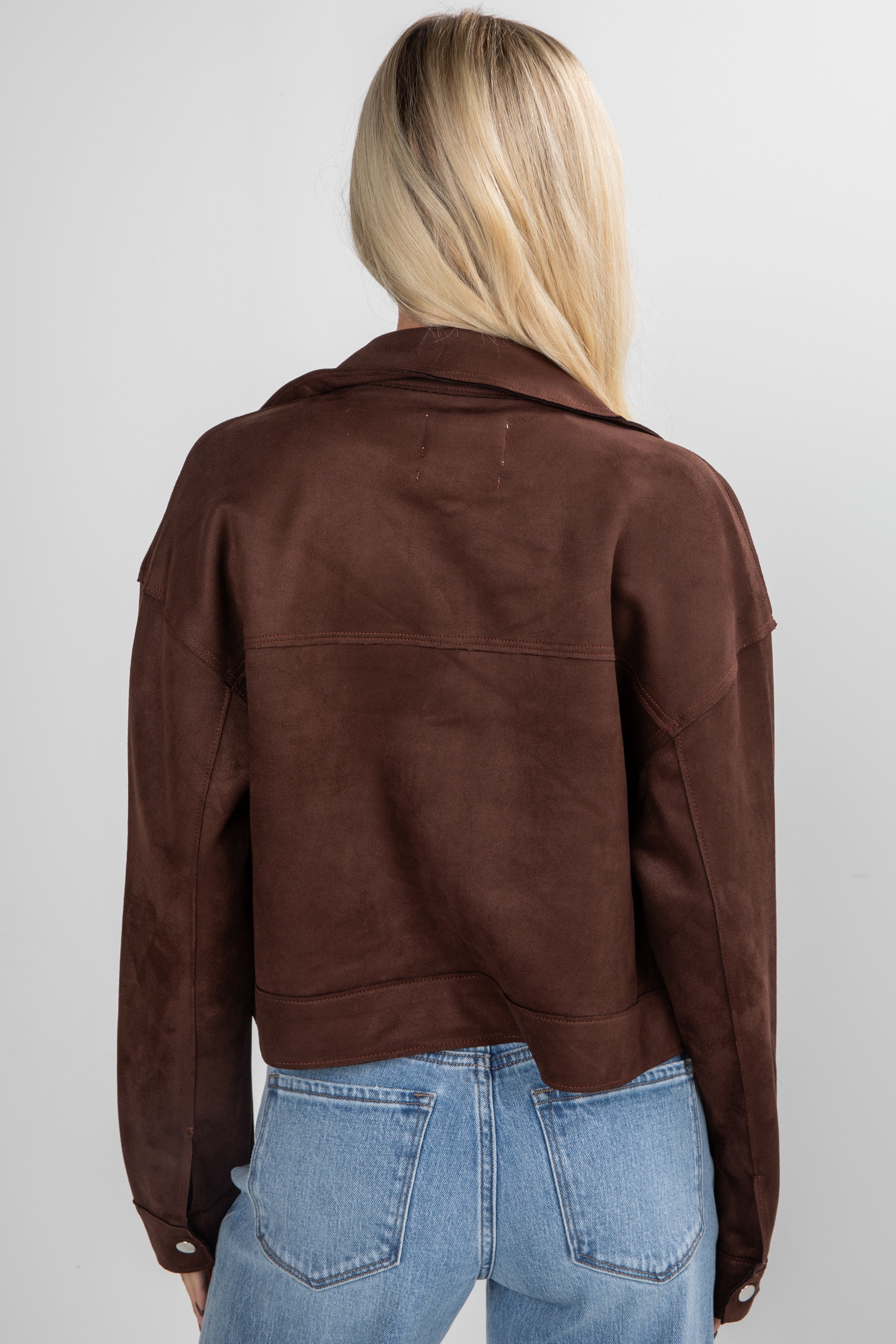 Person wearing a brown jacket and blue jeans on a plain background