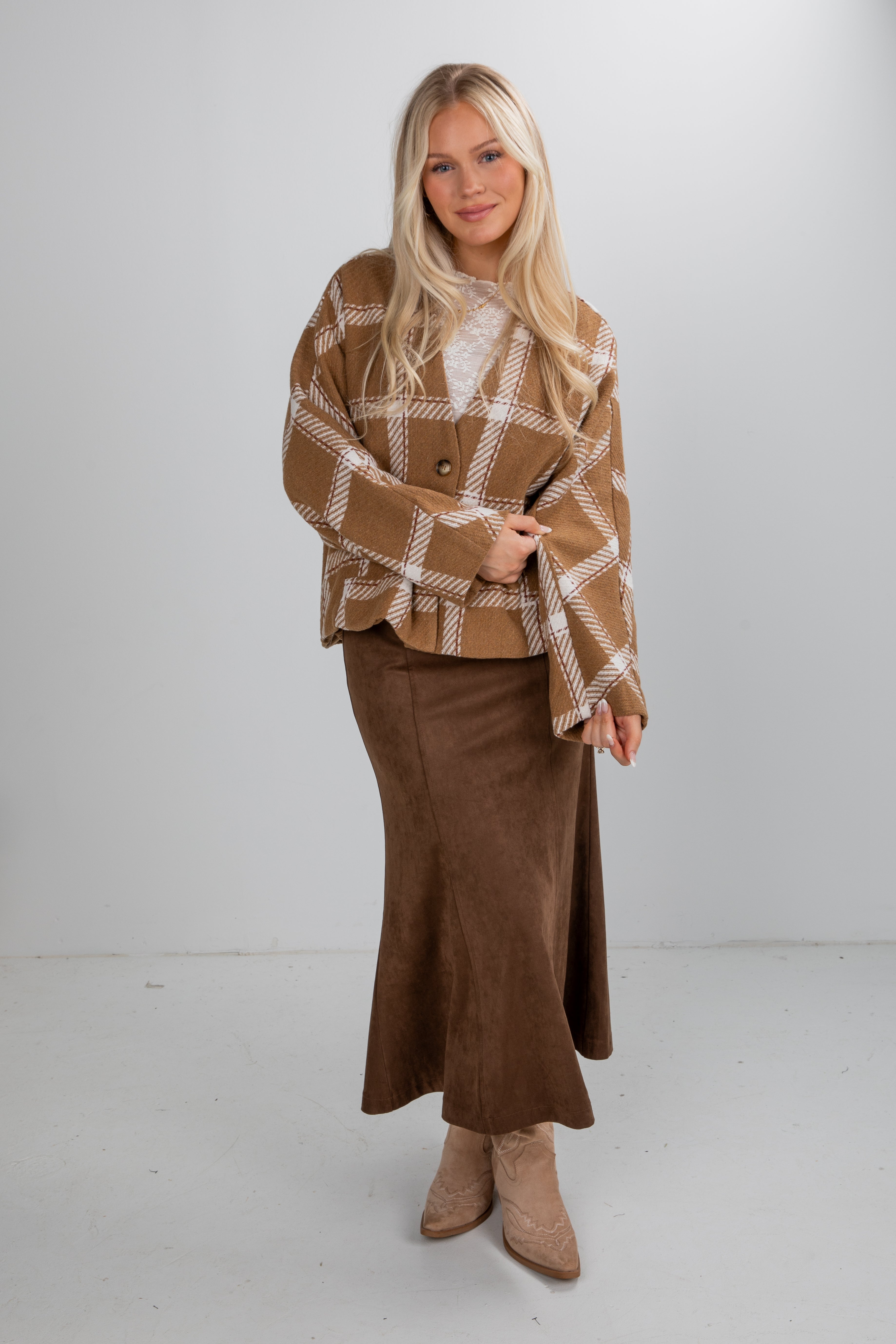 Woman wearing a brown plaid jacket and brown skirt against a white background