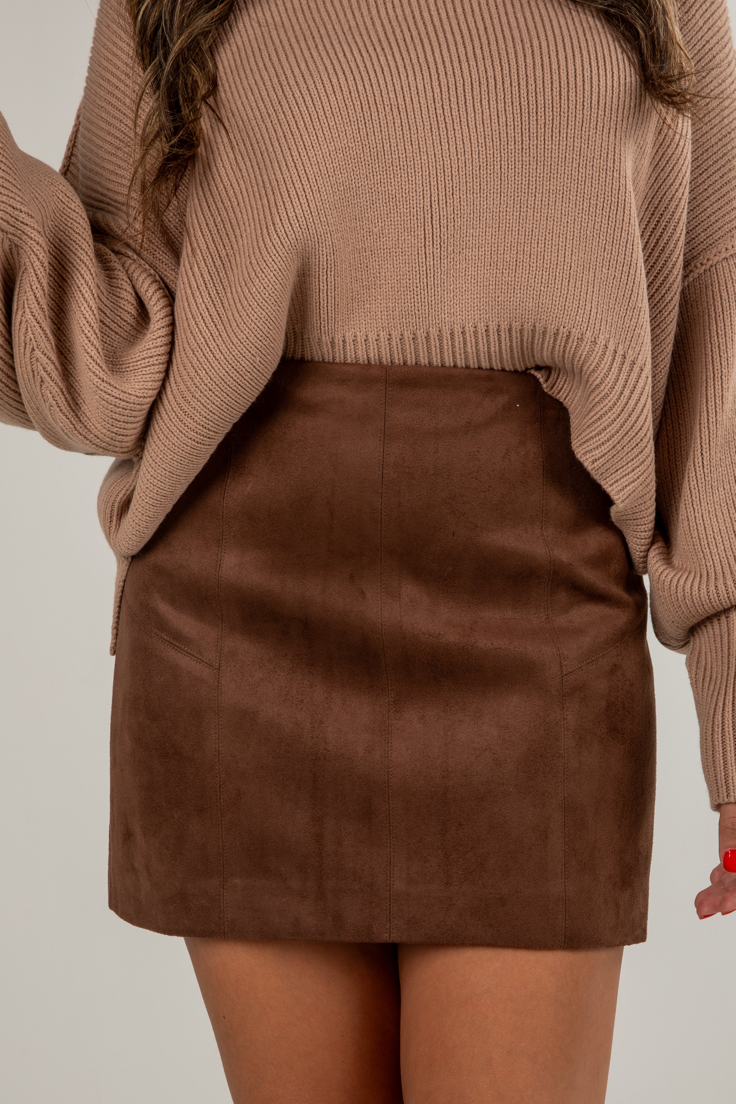 Person wearing a brown sweater and suede skirt on a plain background