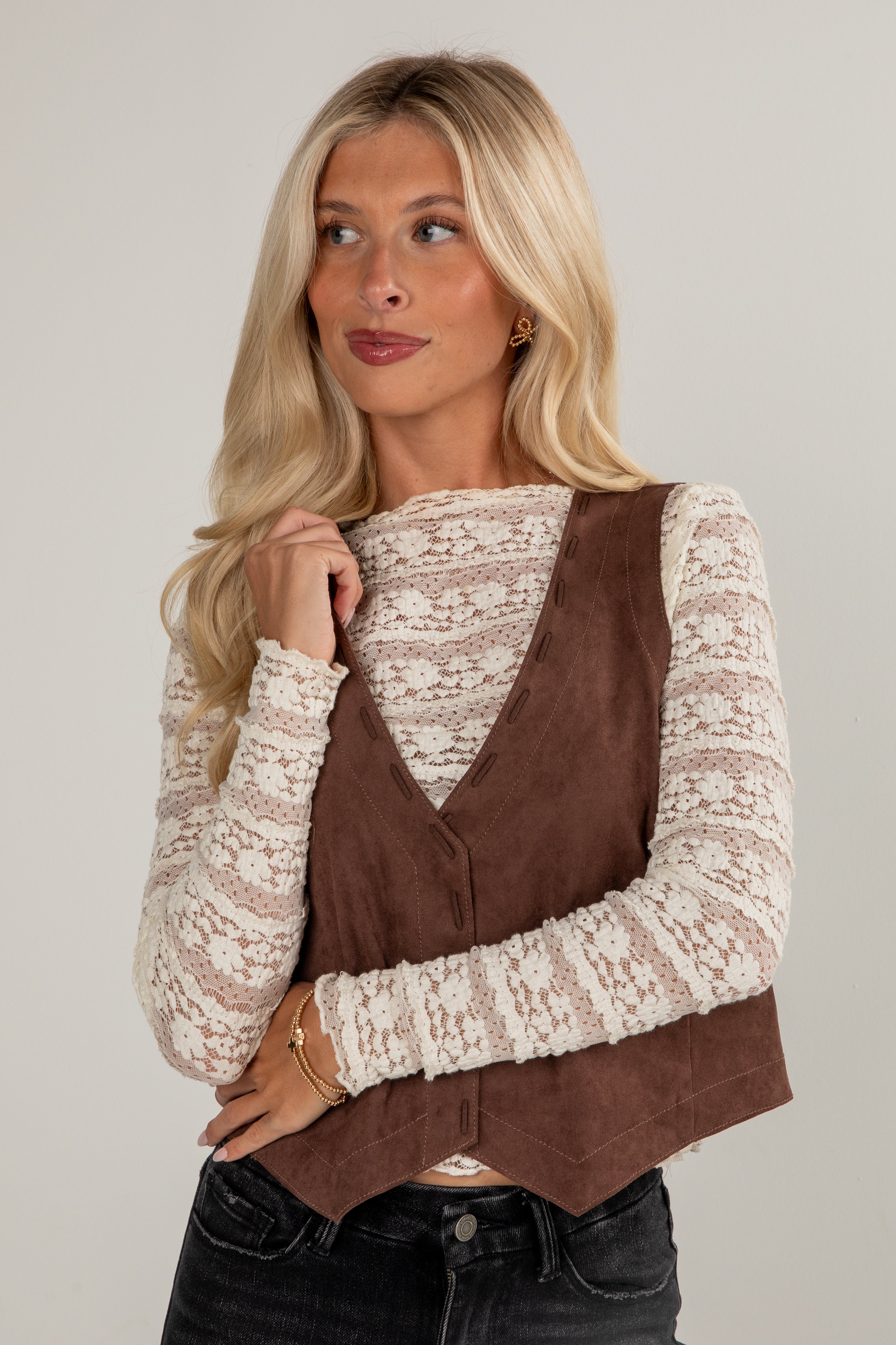 Woman wearing a brown suede vest over a patterned top on a plain background