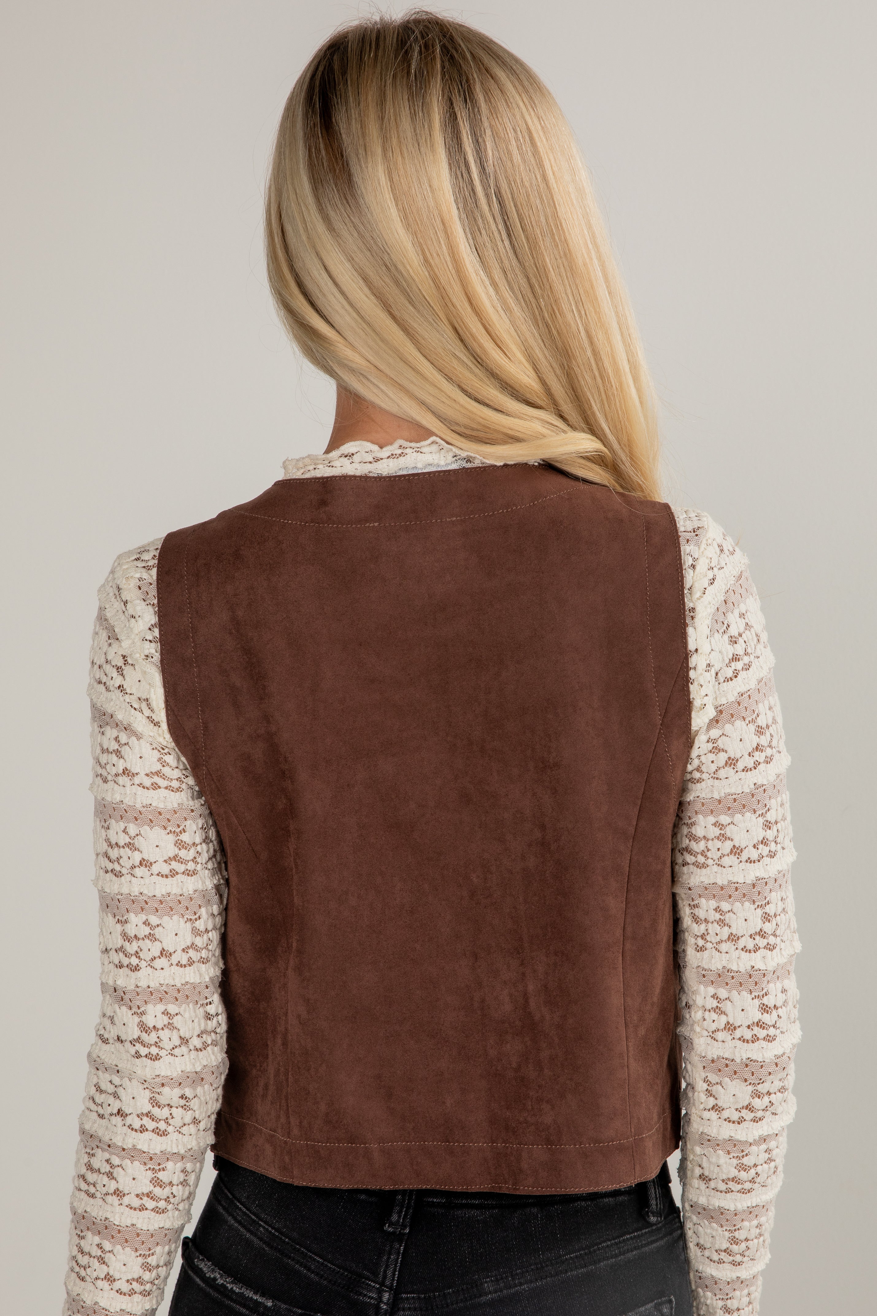 Person wearing a brown suede vest over a patterned shirt on a plain background