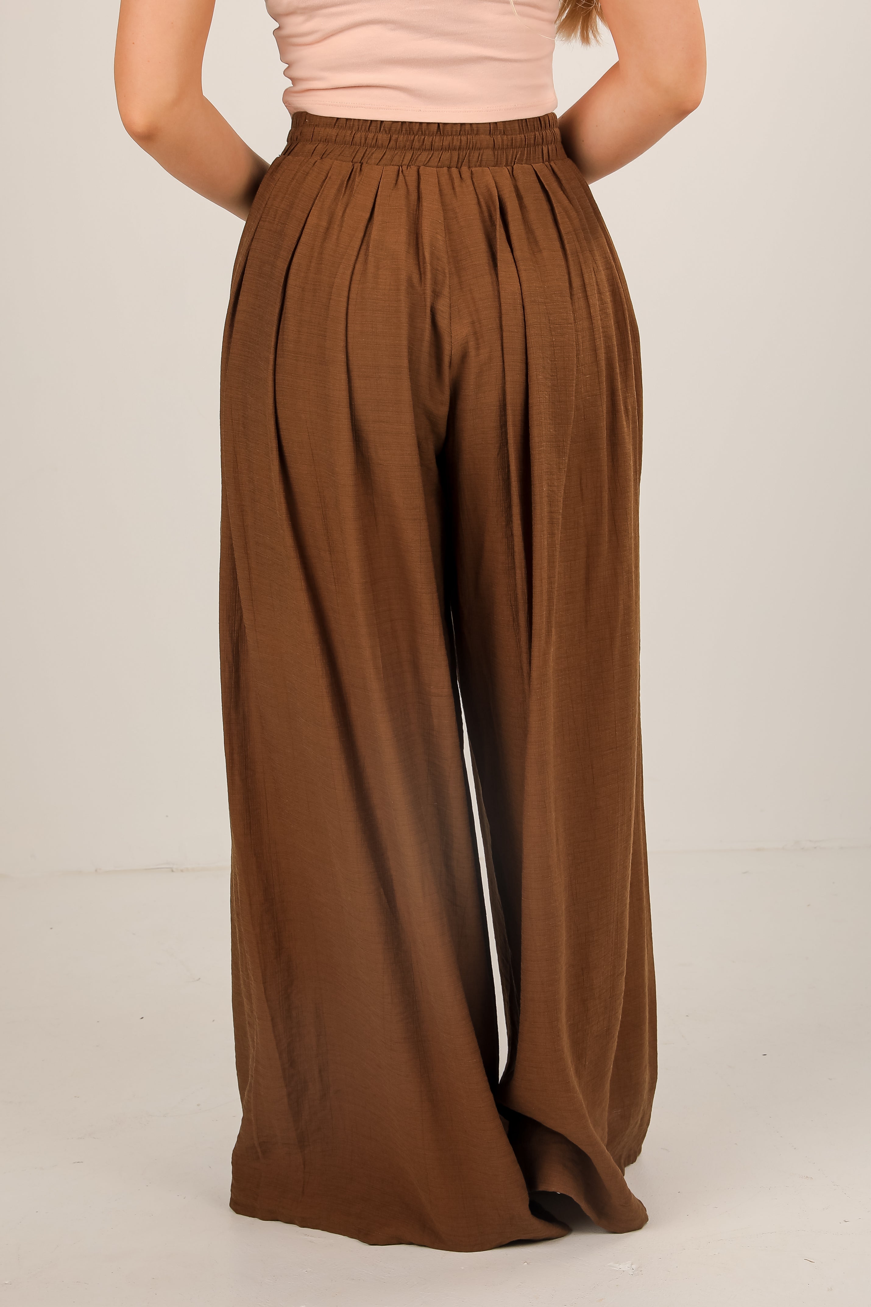 Brown wide-leg pants worn by a person on a beige background