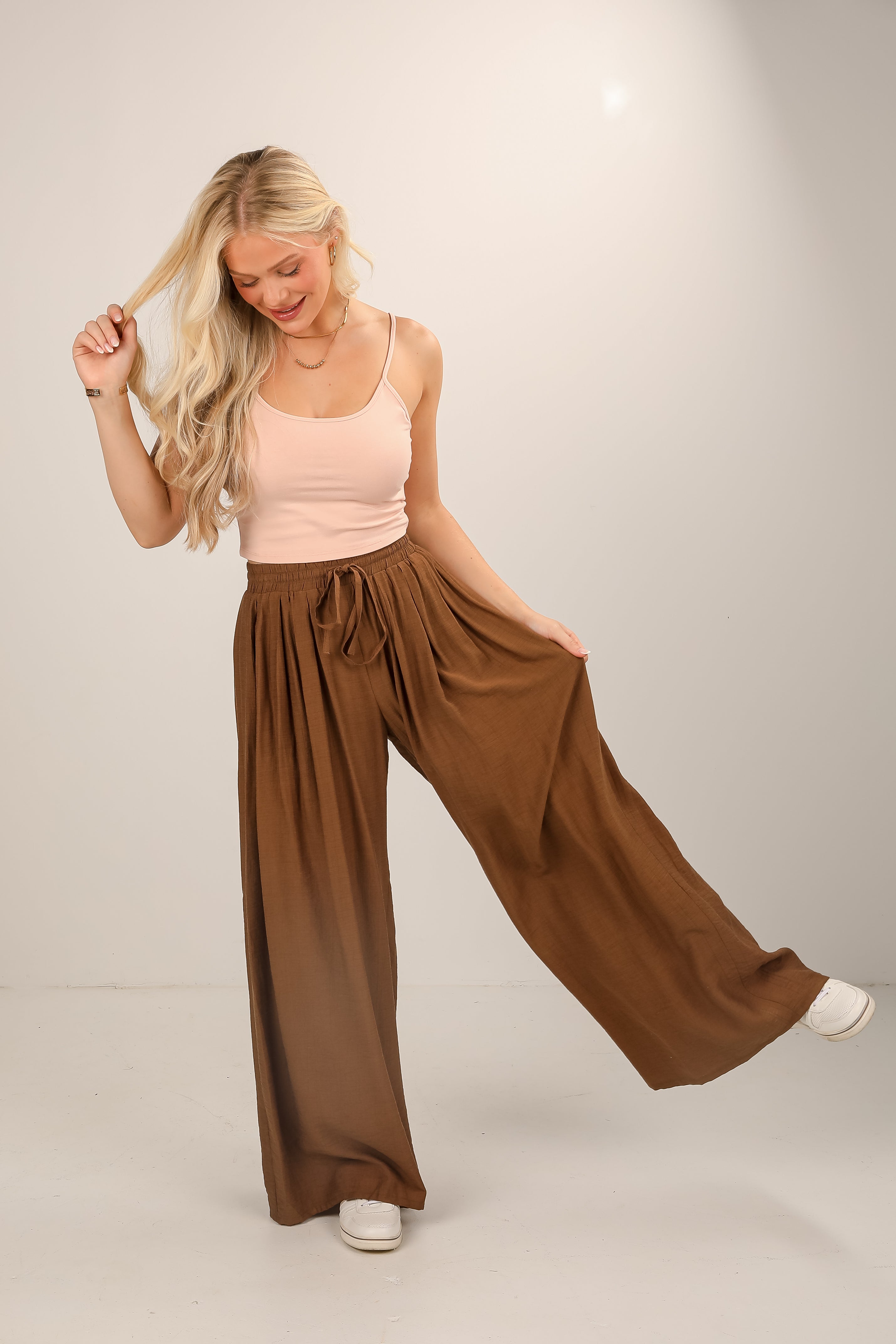 Woman wearing a pink top and brown wide-leg pants on a plain background