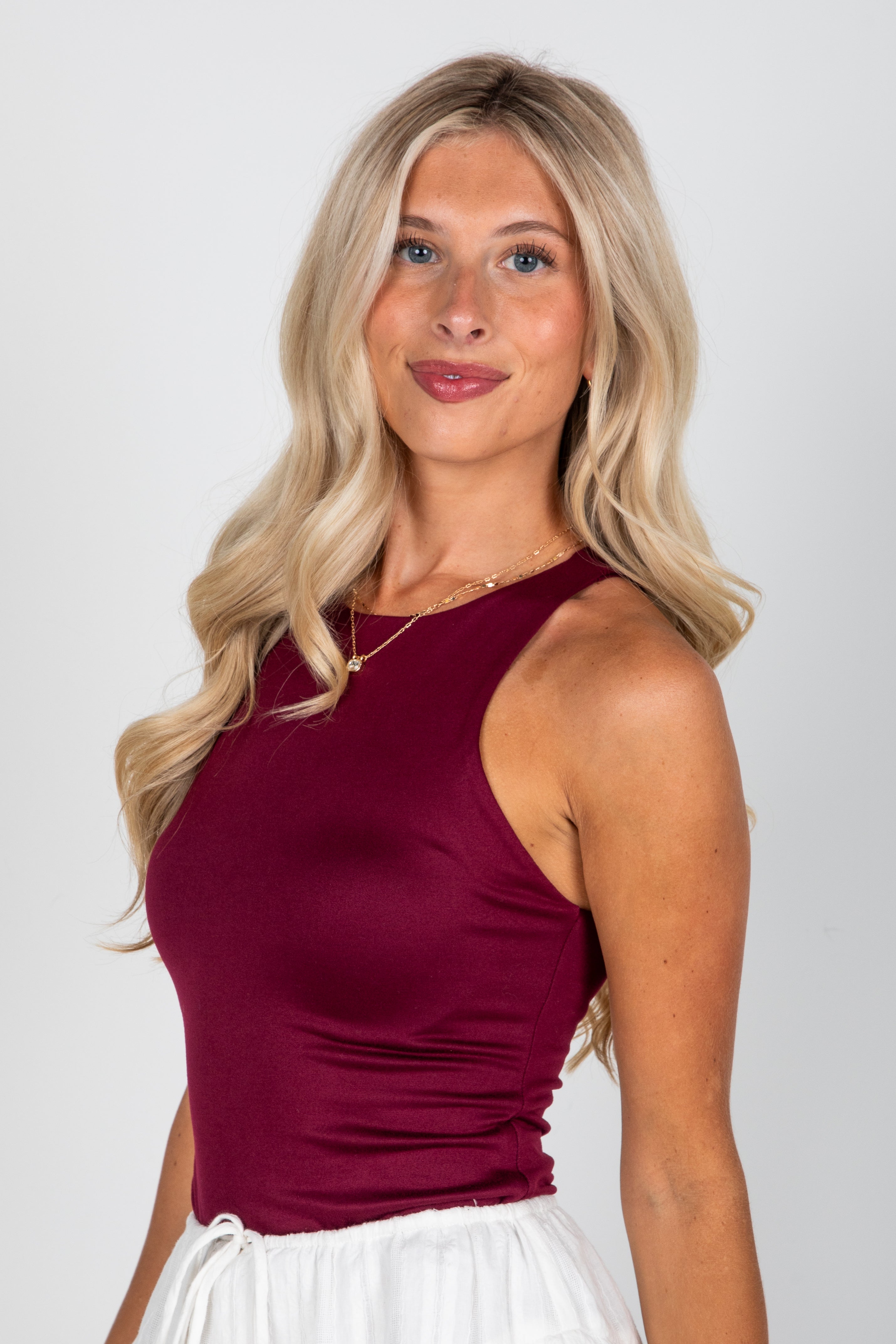 Woman wearing a burgundy top and white skirt against a plain background