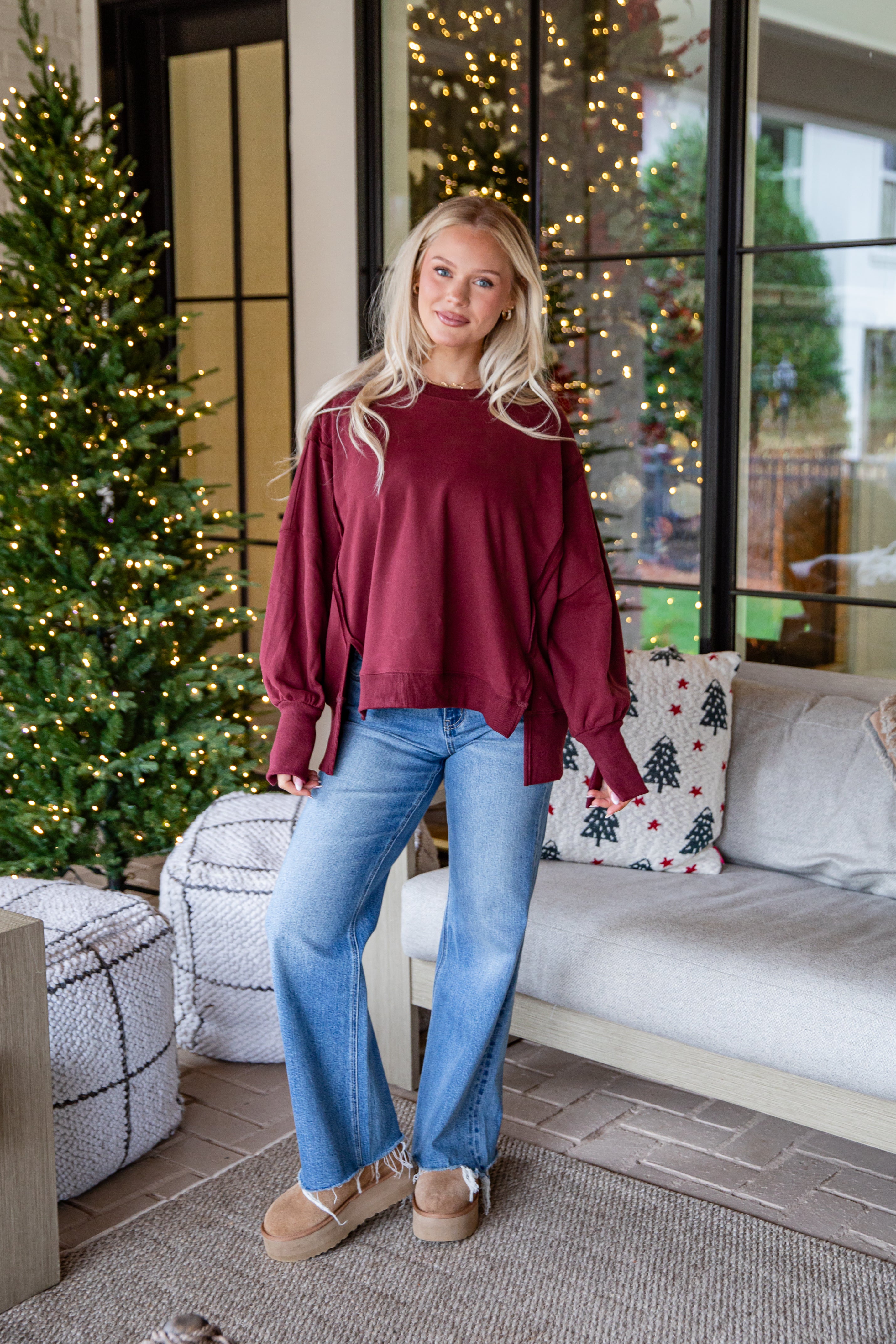 Woman in a burgundy sweater and blue jeans standing in a living room with Christmas decorations.