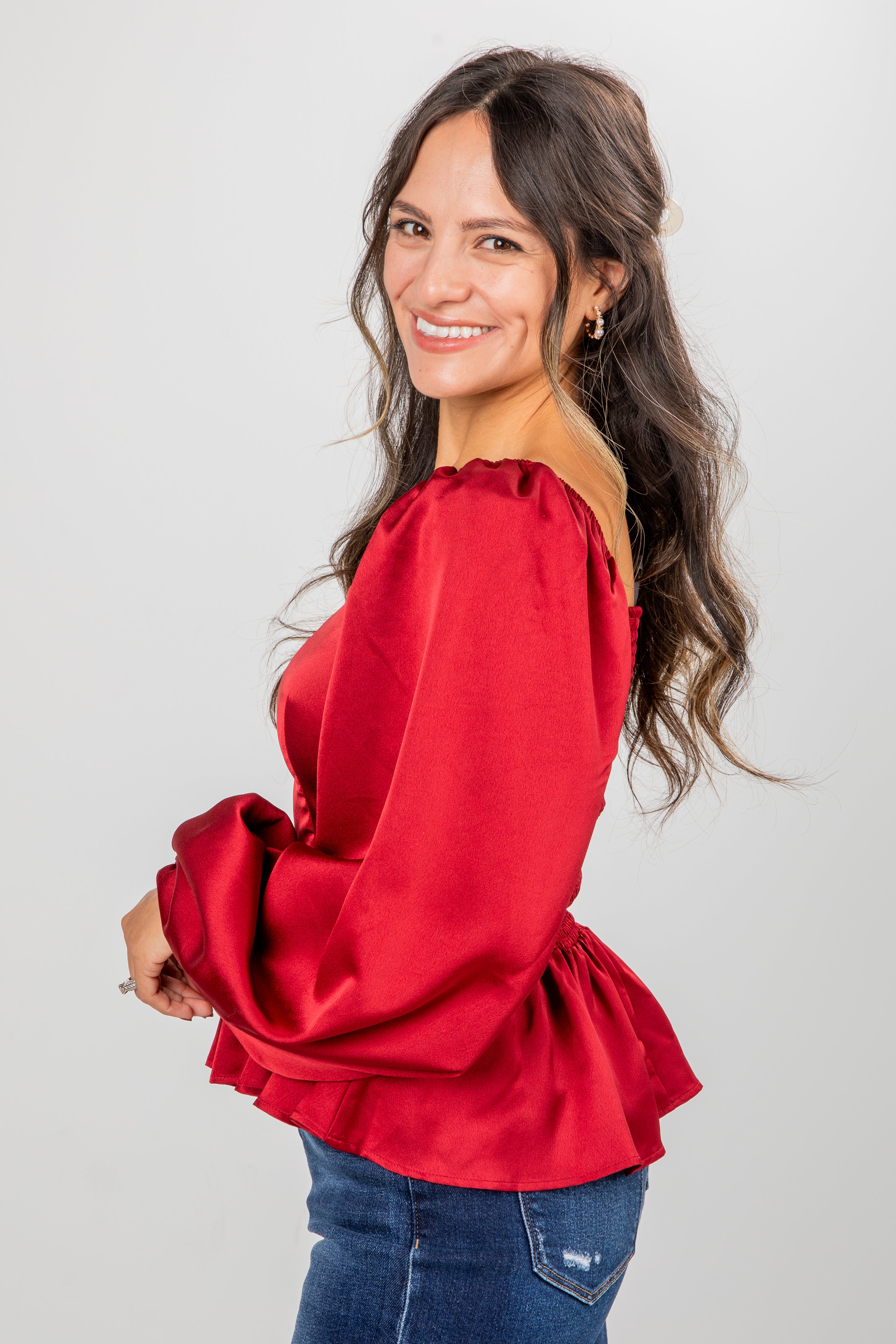Woman wearing a red blouse with blue jeans on a plain background