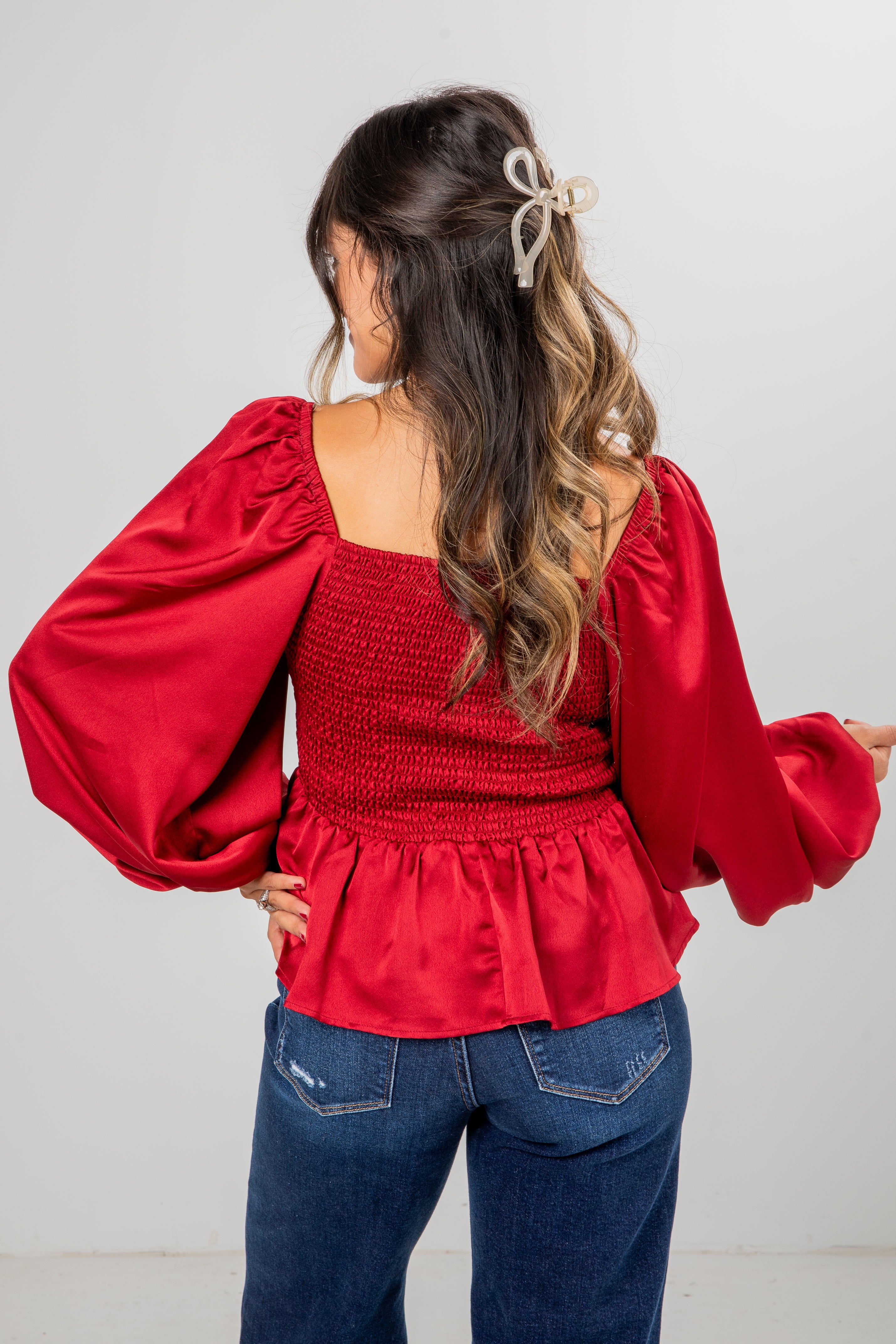 Woman wearing a red blouse with balloon sleeves and blue jeans on a plain background