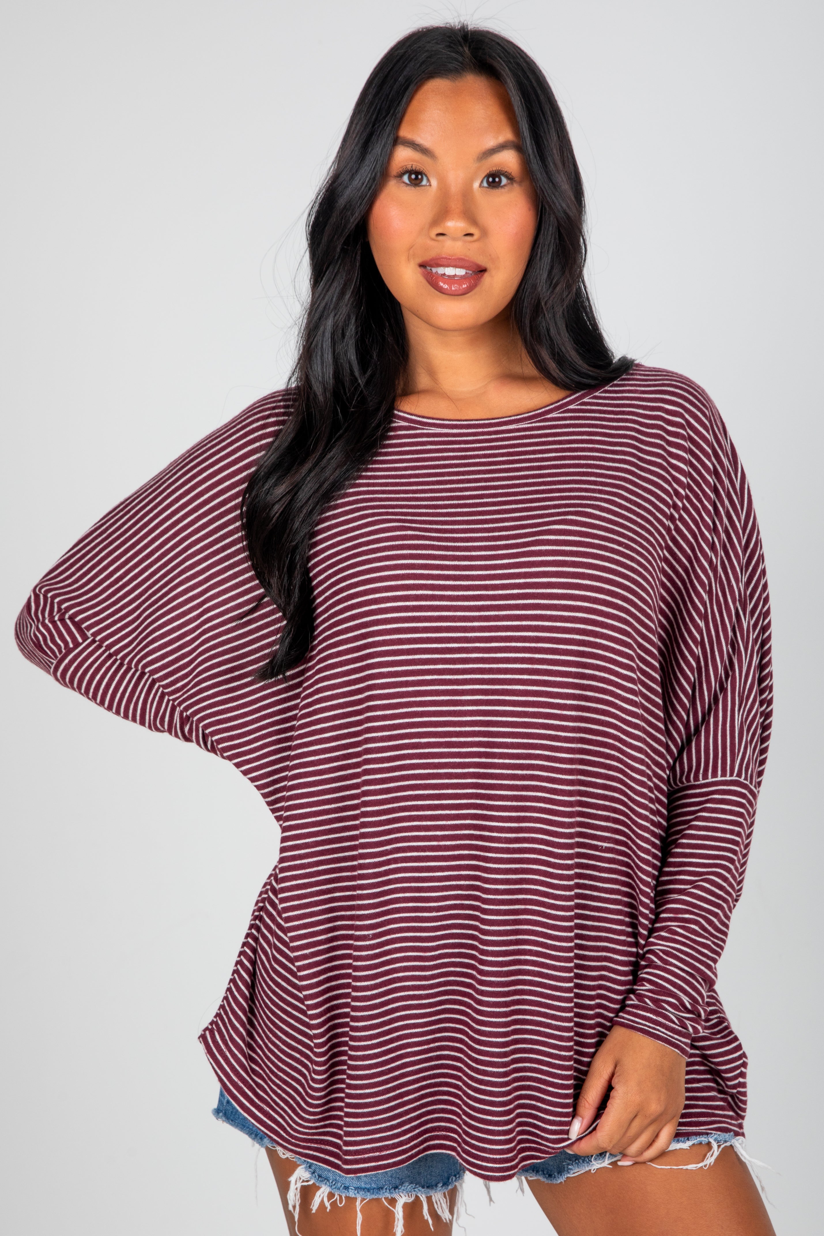 Woman wearing a maroon and white striped long-sleeve top on a gray background