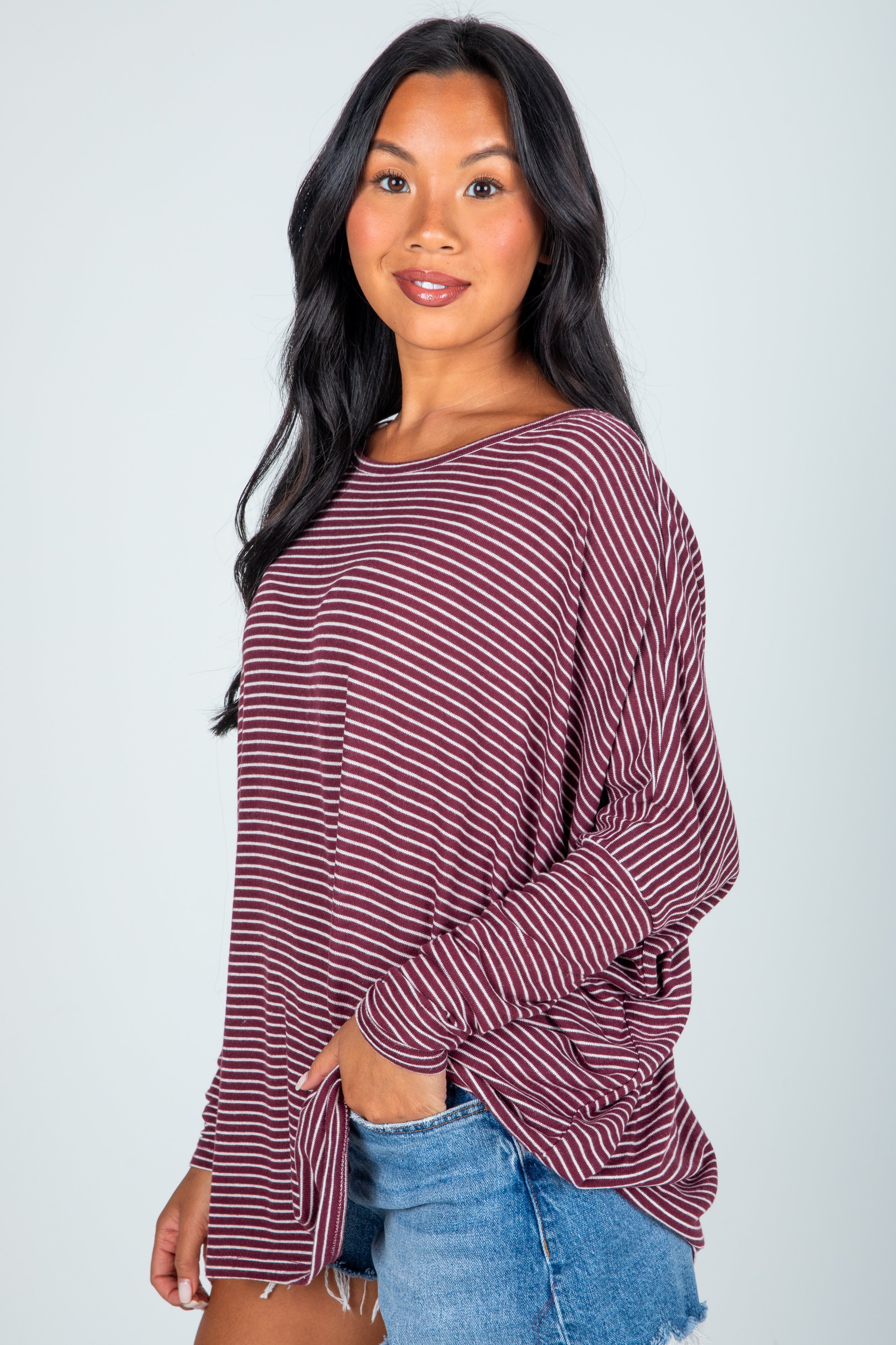 Woman wearing a maroon and white striped top with a knot detail, standing against a plain background.