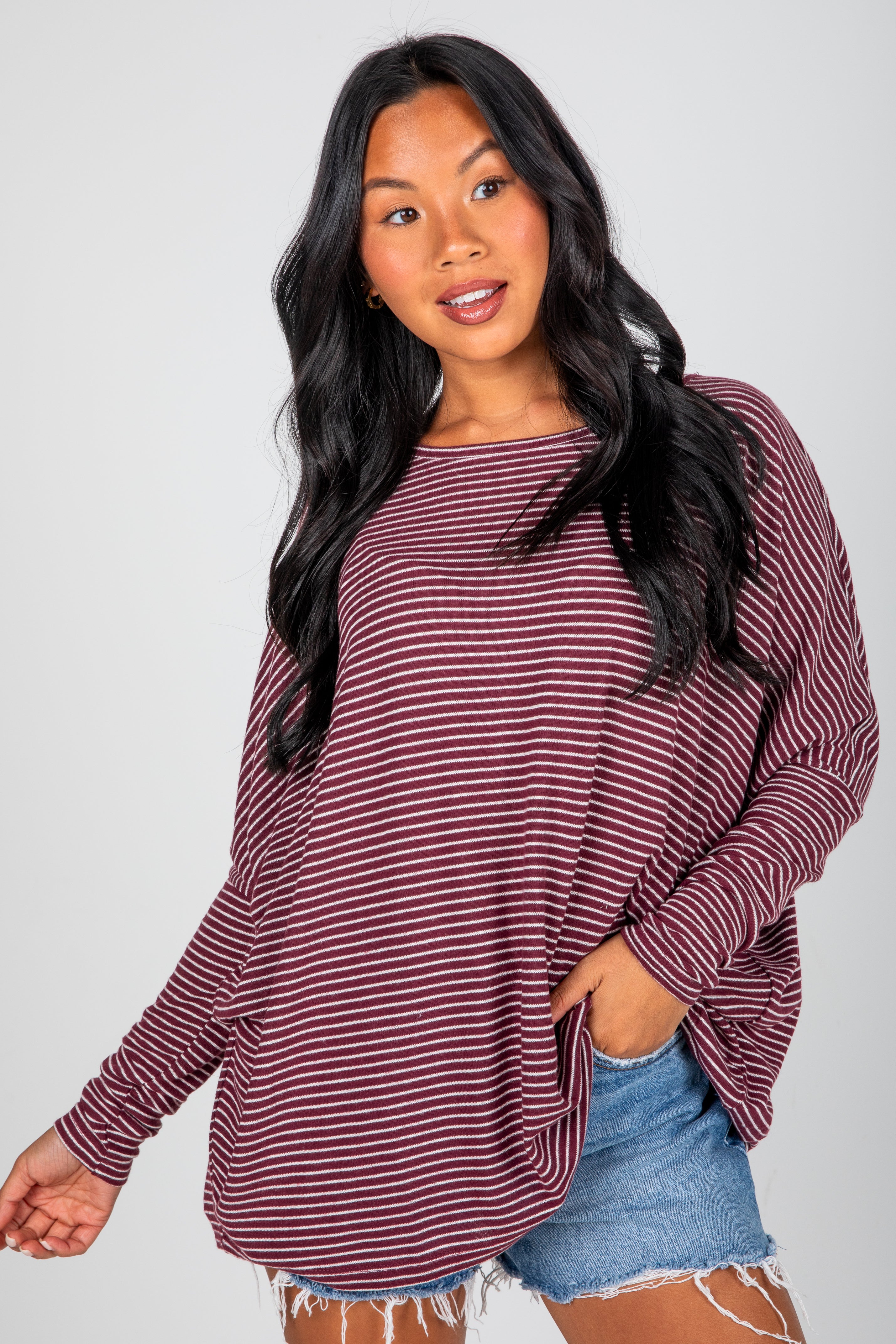 Woman wearing a maroon and white striped long-sleeve top with denim shorts on a plain background
