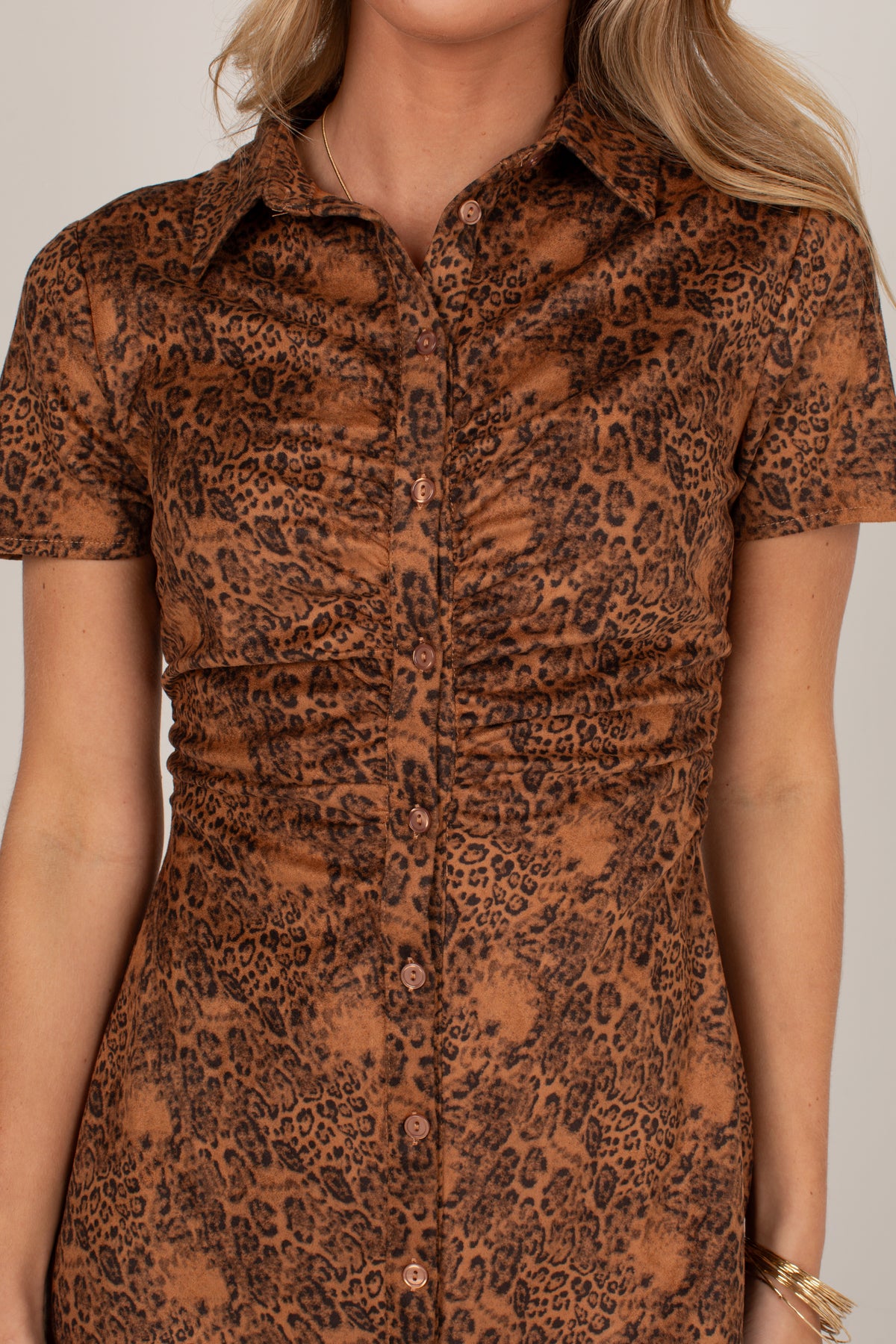 A close-up of a woman wearing a short-sleeve button-front shirt dress with a brown and black leopard print pattern against a light gray background.
