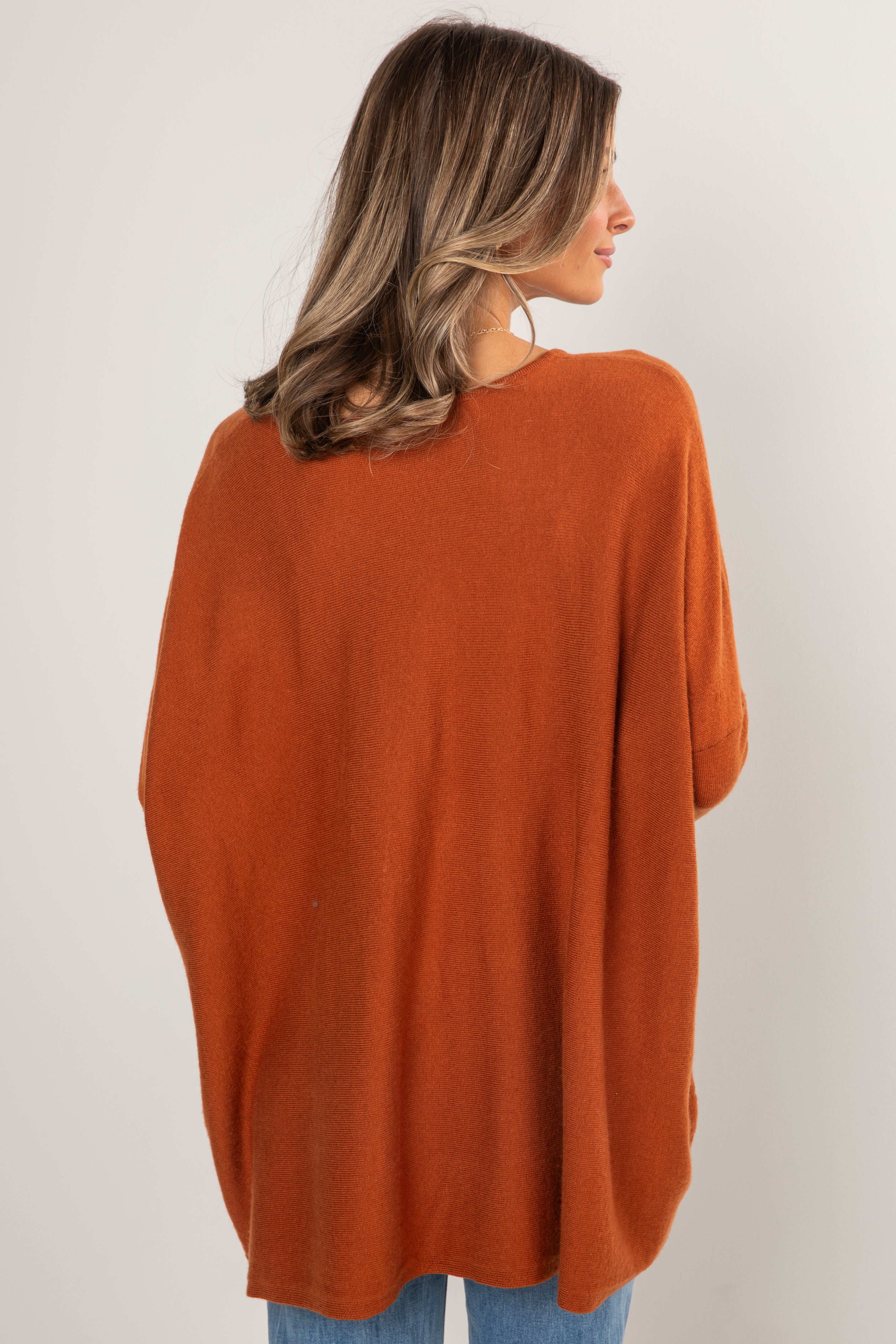 Person wearing a rust-colored sweater against a white background