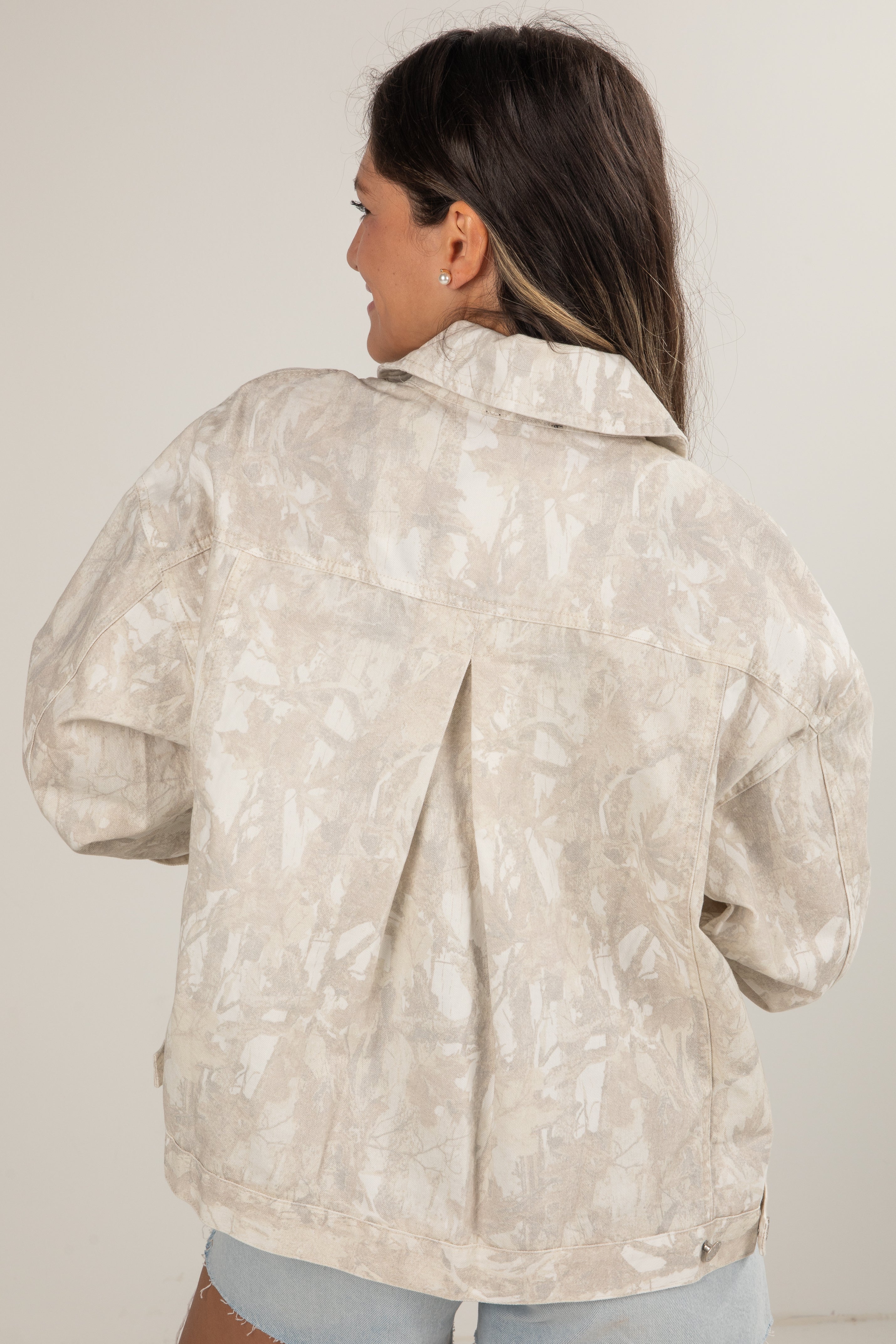 Woman wearing a light-colored floral patterned jacket against a plain background