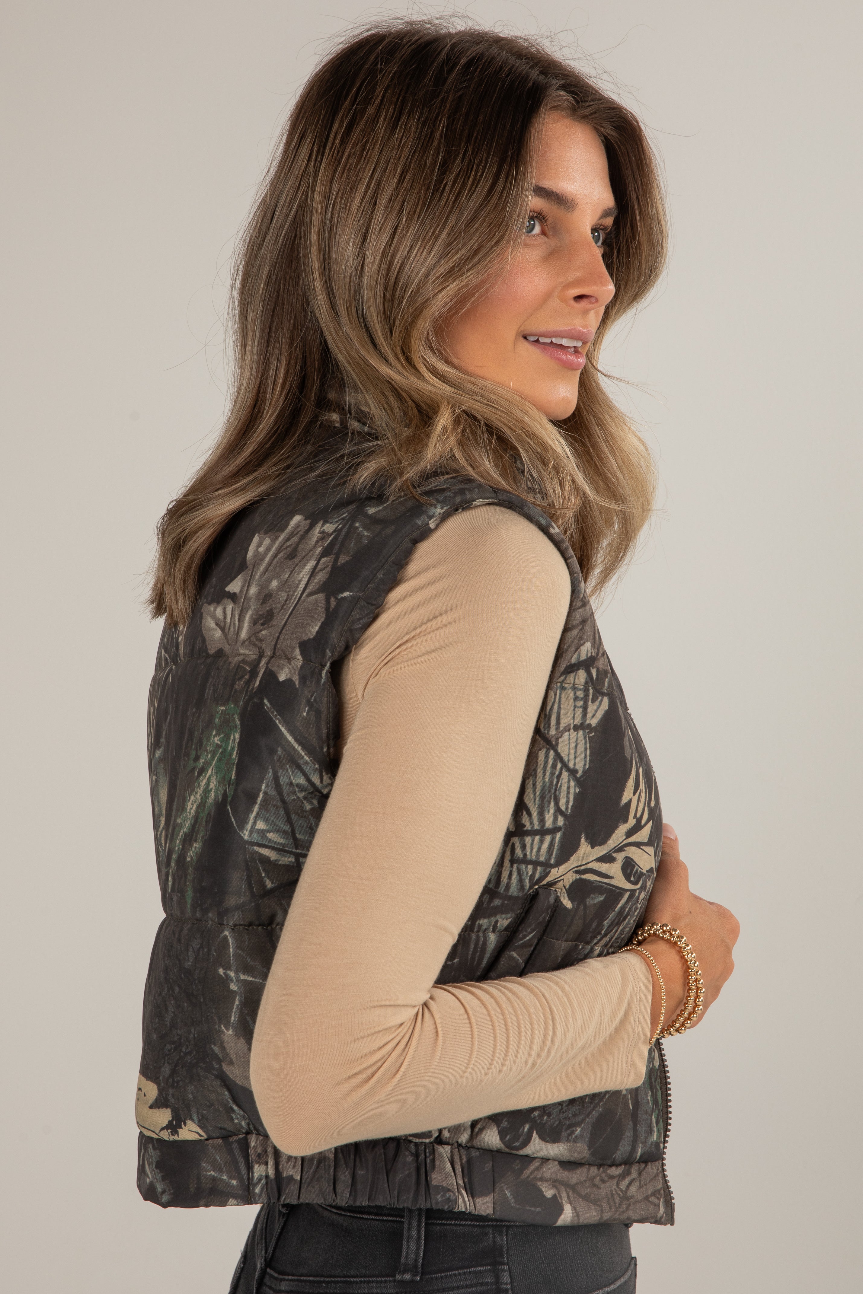 Woman wearing a camouflage vest against a plain background