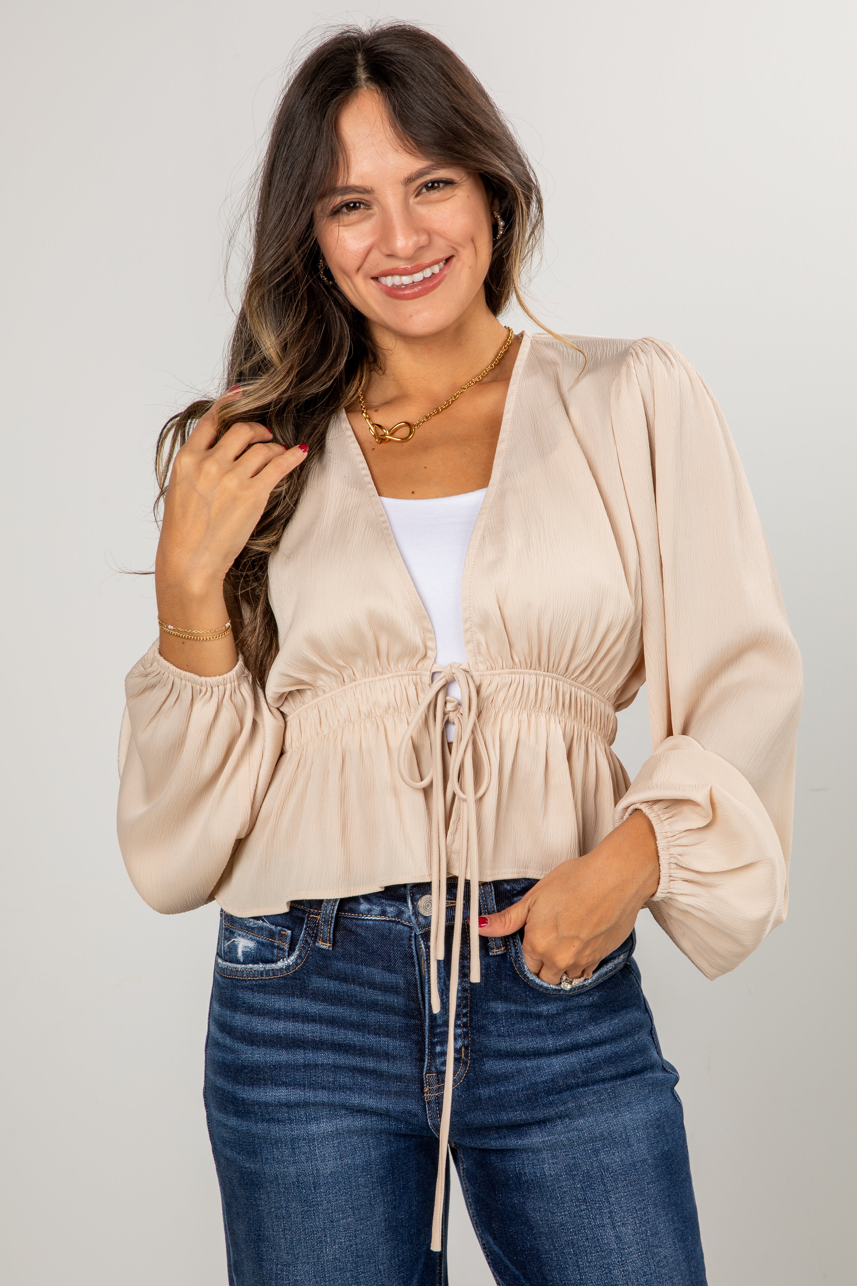 Woman wearing a beige blouse and blue jeans against a plain background