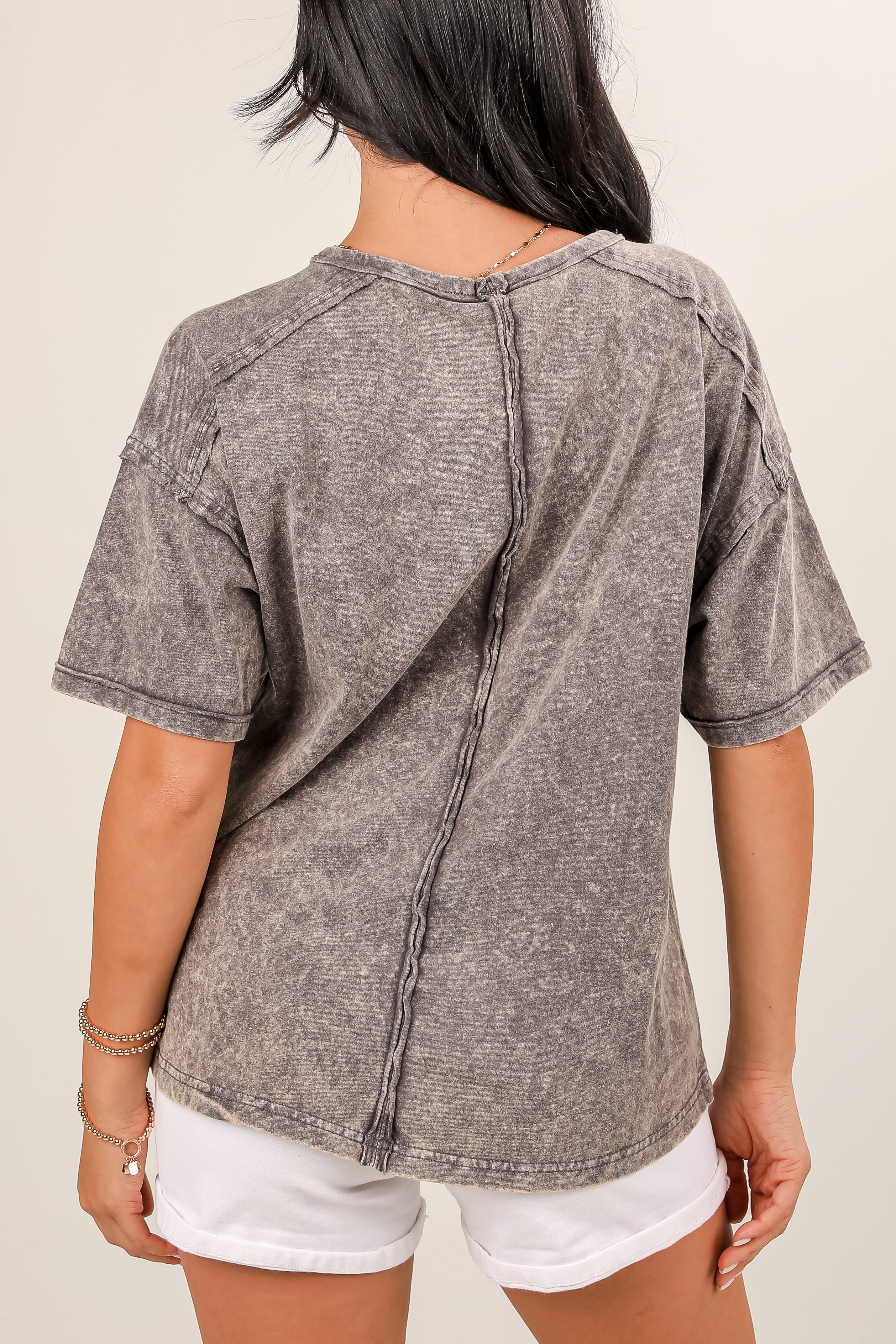 Person wearing a gray distressed denim shirt with white shorts on a plain background