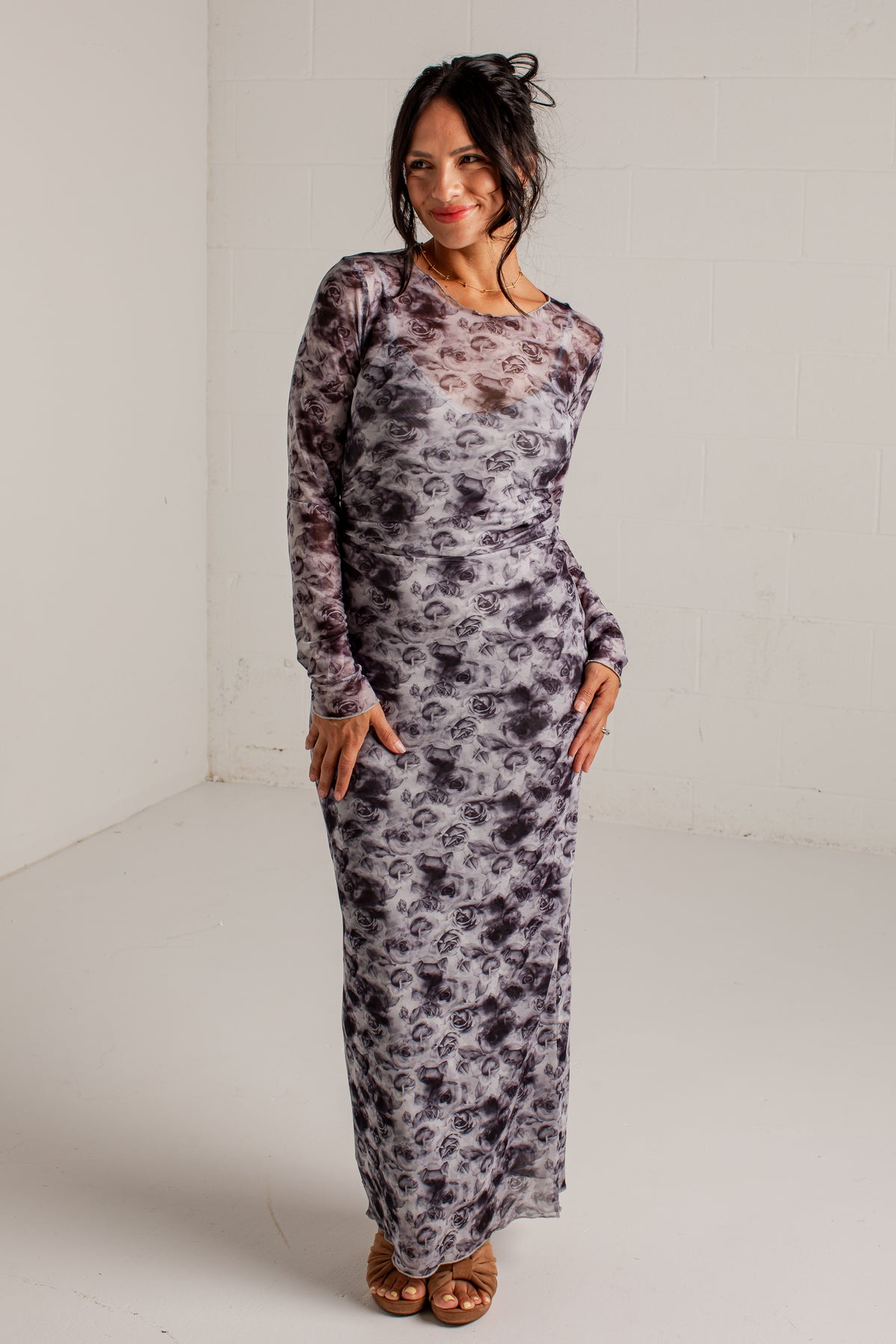 A woman modeling a long-sleeve maxi dress with a gray and black abstract floral pattern, standing in a white studio corner.