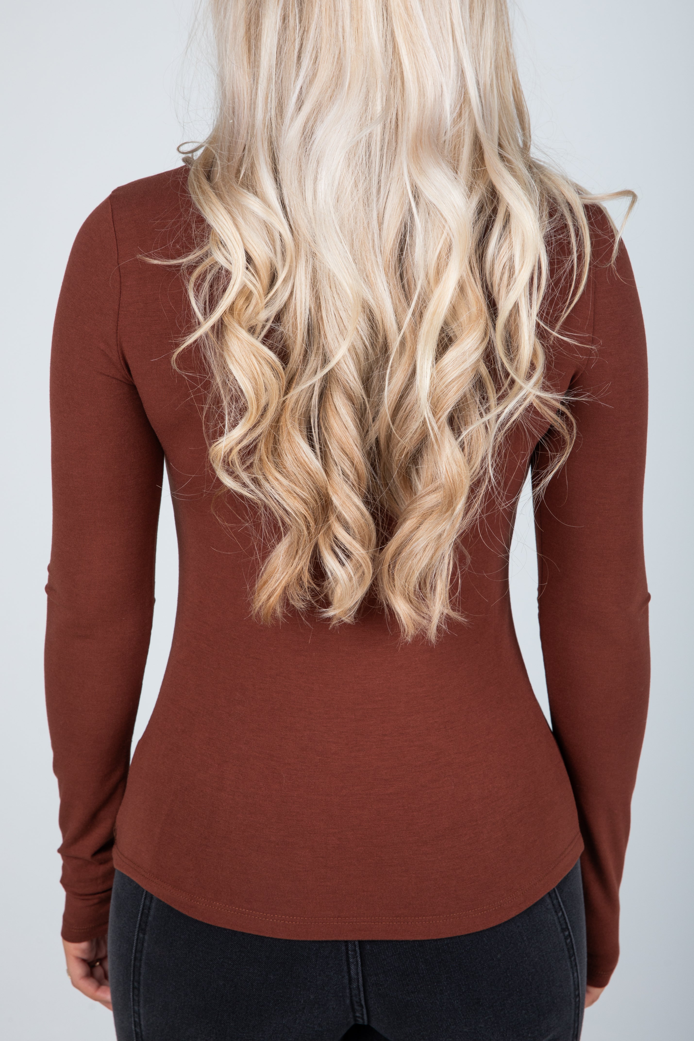 Person wearing a brown long-sleeve top with a plain background