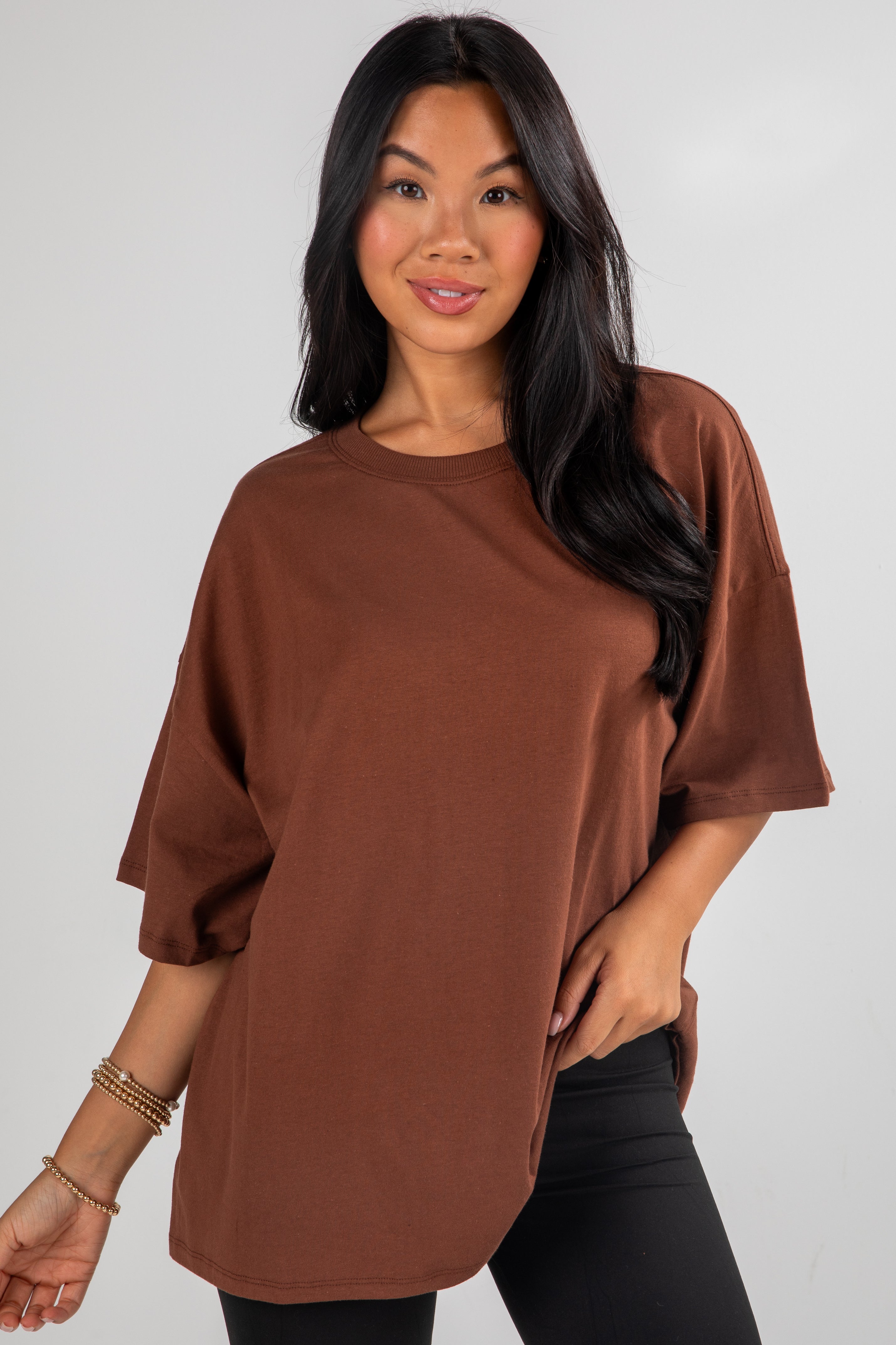 Woman wearing a brown oversized t-shirt against a plain background