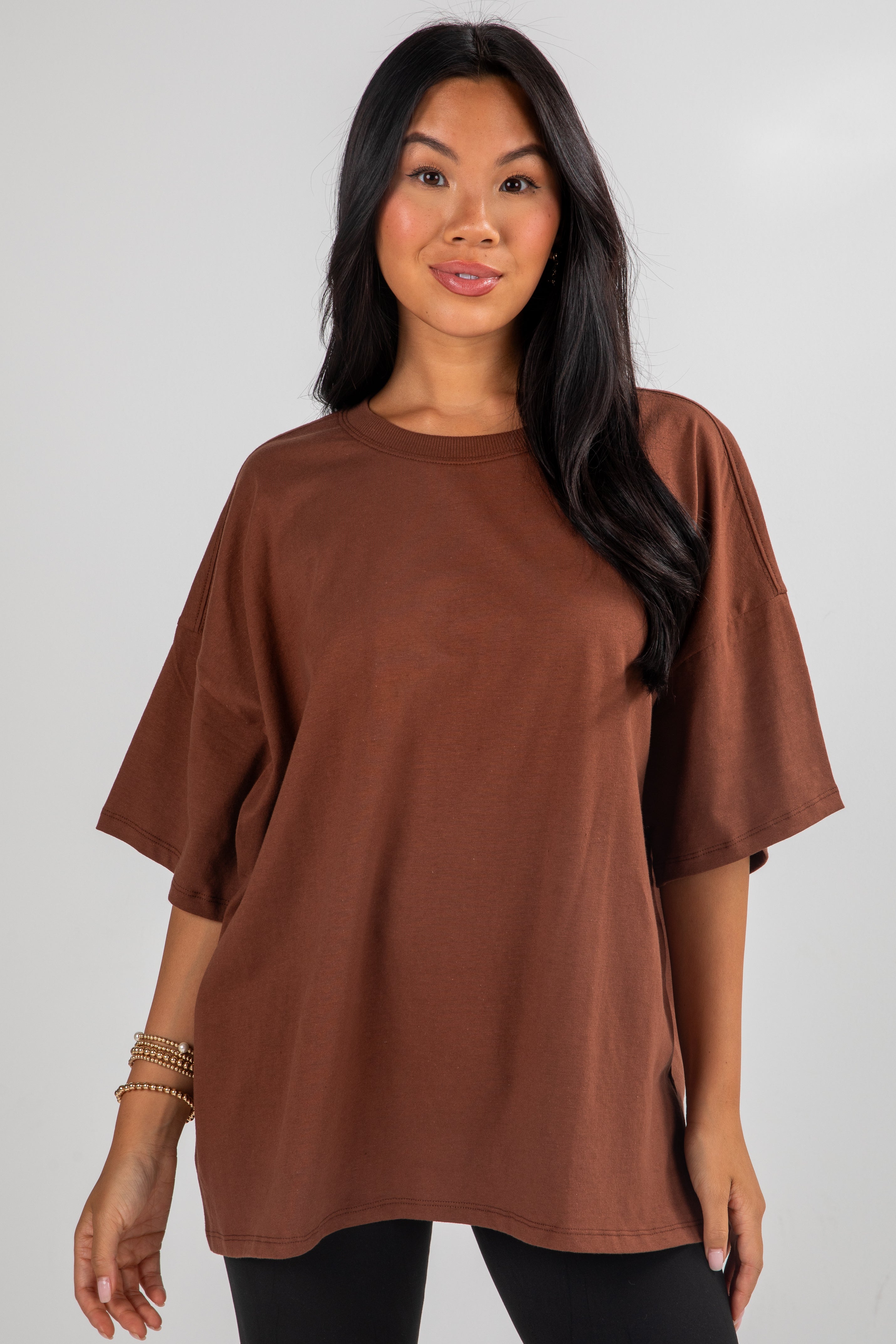 Woman wearing a brown oversized t-shirt against a plain background