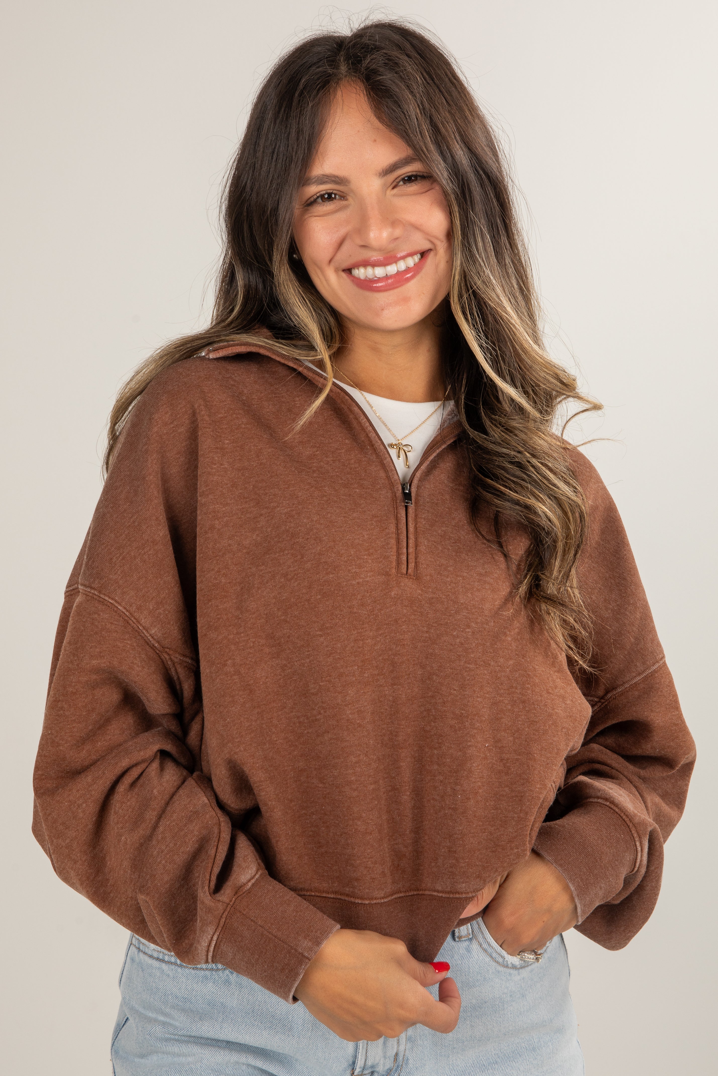 Woman wearing a brown zip-up sweatshirt against a plain background