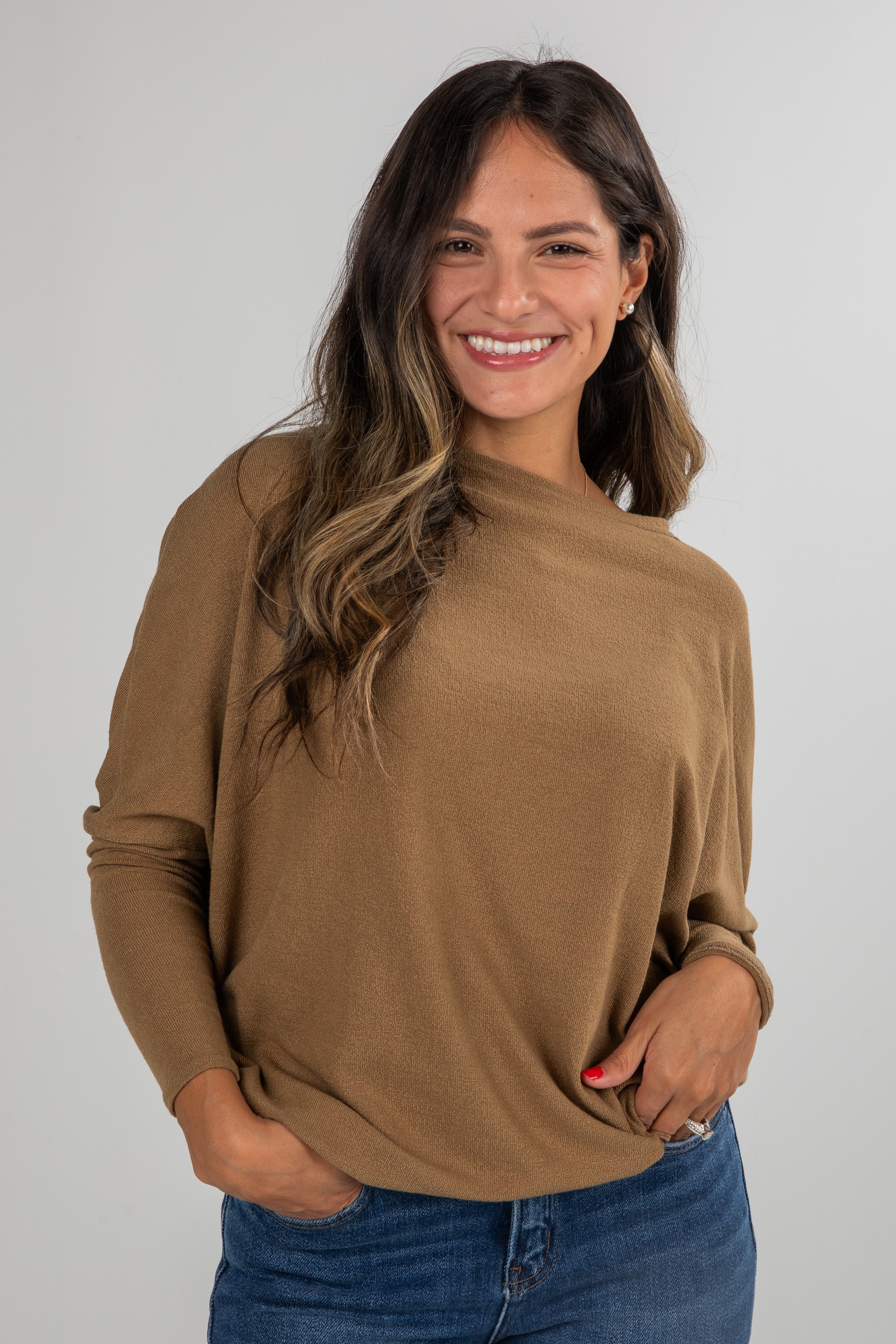 Woman wearing a brown sweater and blue jeans against a plain background